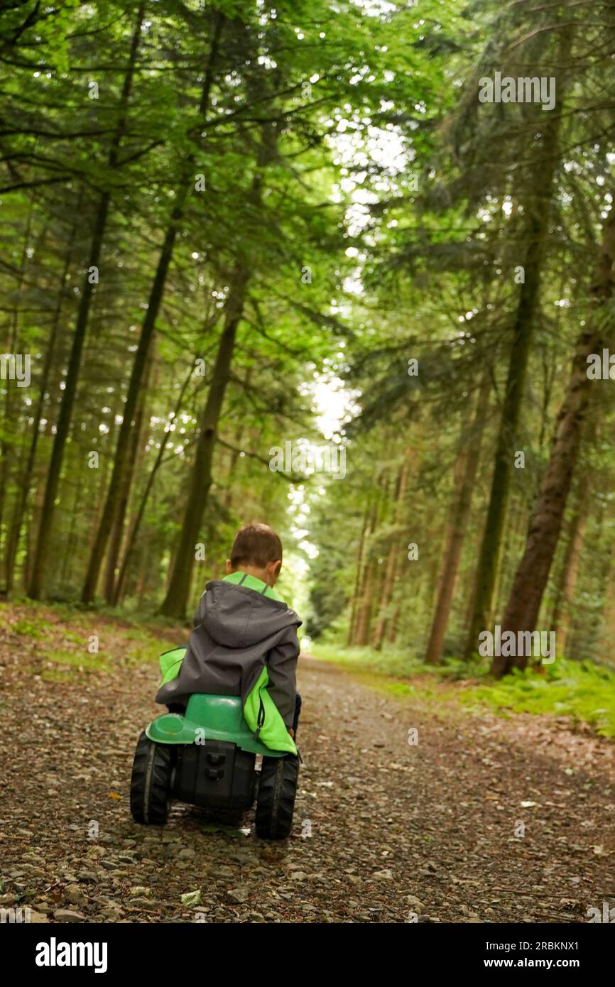 Ein kleiner Junge fährt in einem Spielzeugauto durch einen dichten Wald in die Ferne. Das Kind geht in eine unbekannte Zukunft. Lebensweg, Lebenswegkonzept. Stockfoto