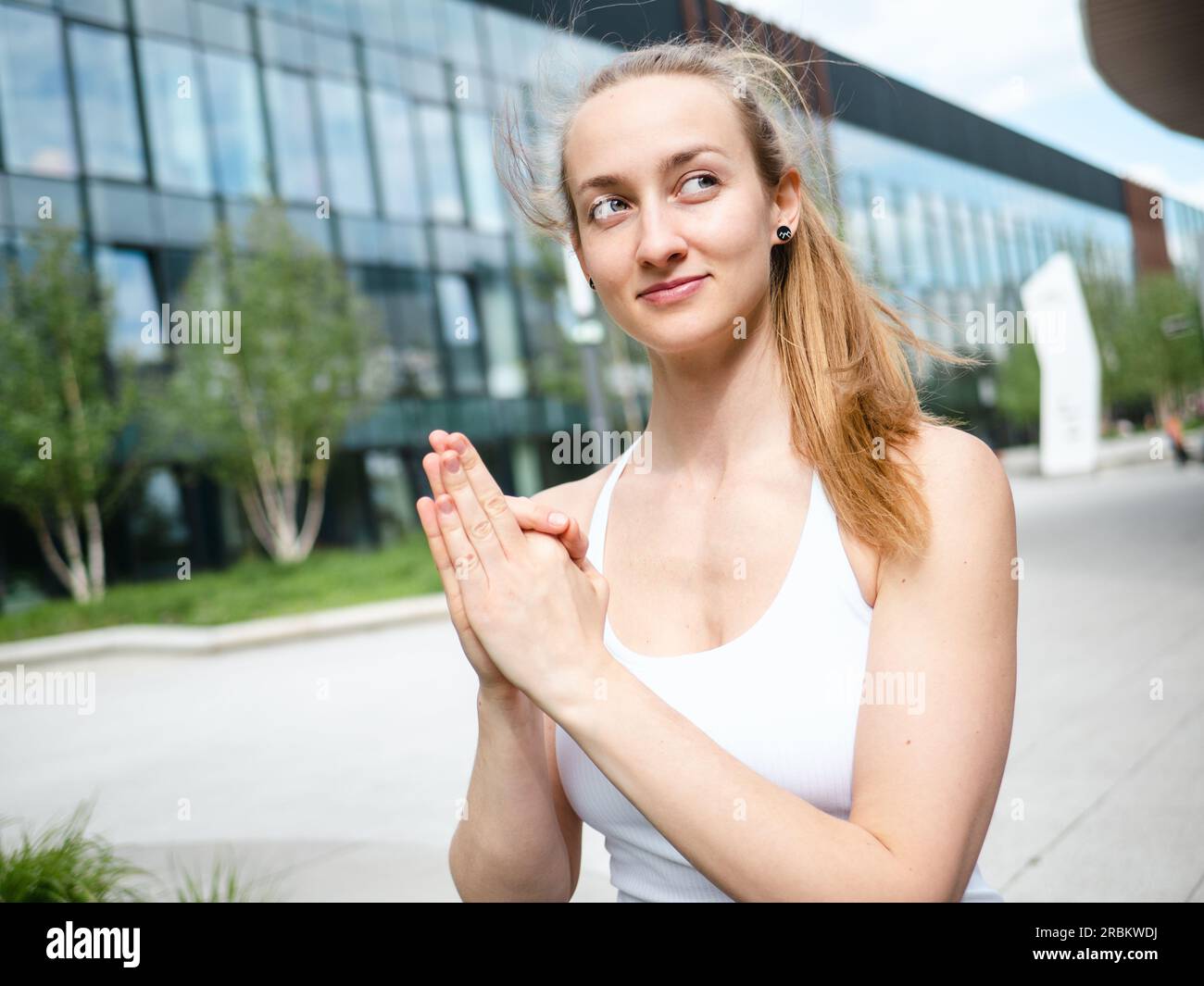Junge blonde Frau, die an sonnigen Sommertagen Yoga Mudra im Freien macht, mit urbanem Hintergrund und einer schönen Seite Stockfoto