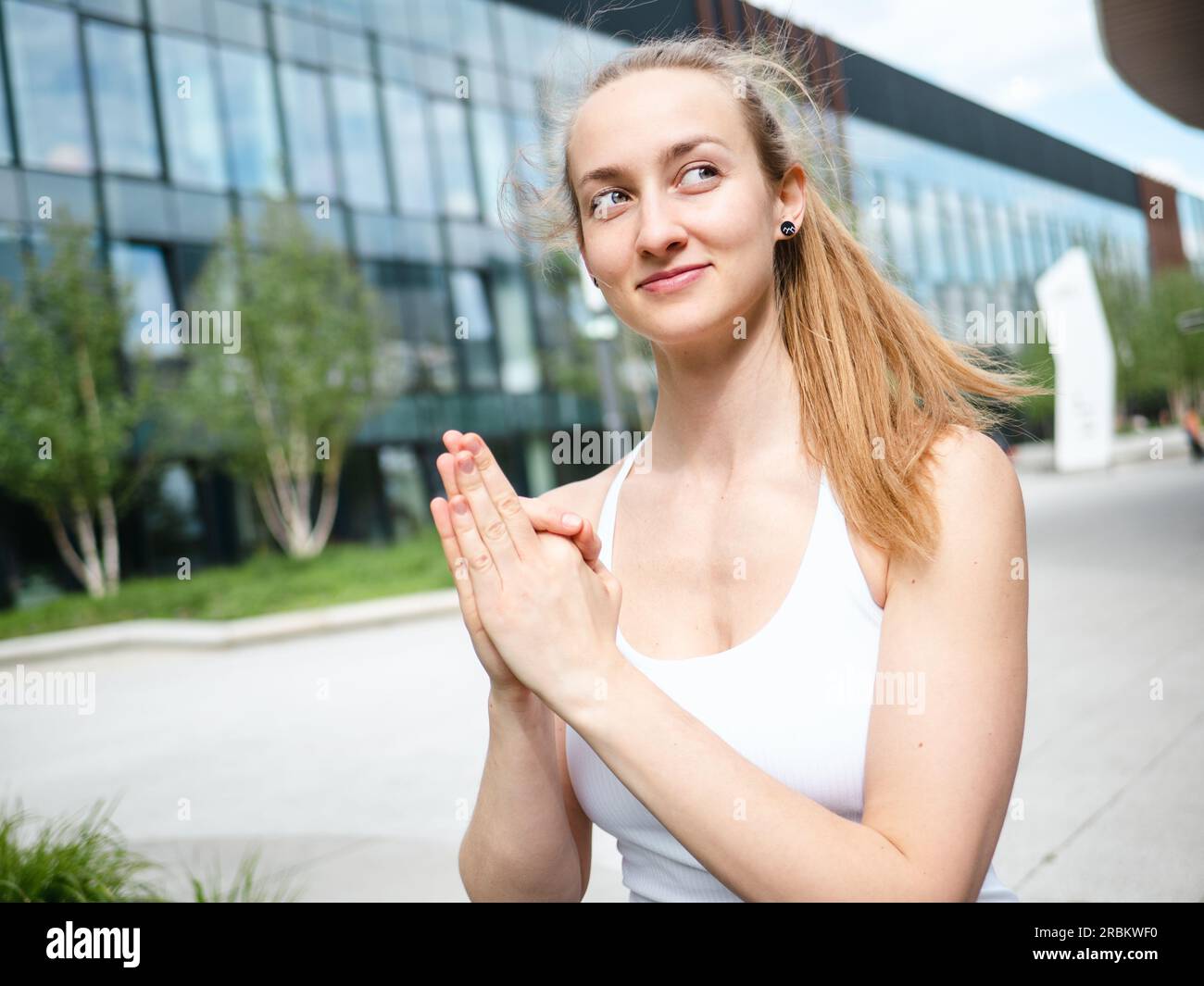 Junge blonde Frau, die an sonnigen Sommertagen Yoga Mudra im Freien macht, mit urbanem Hintergrund und einer schönen Seite Stockfoto