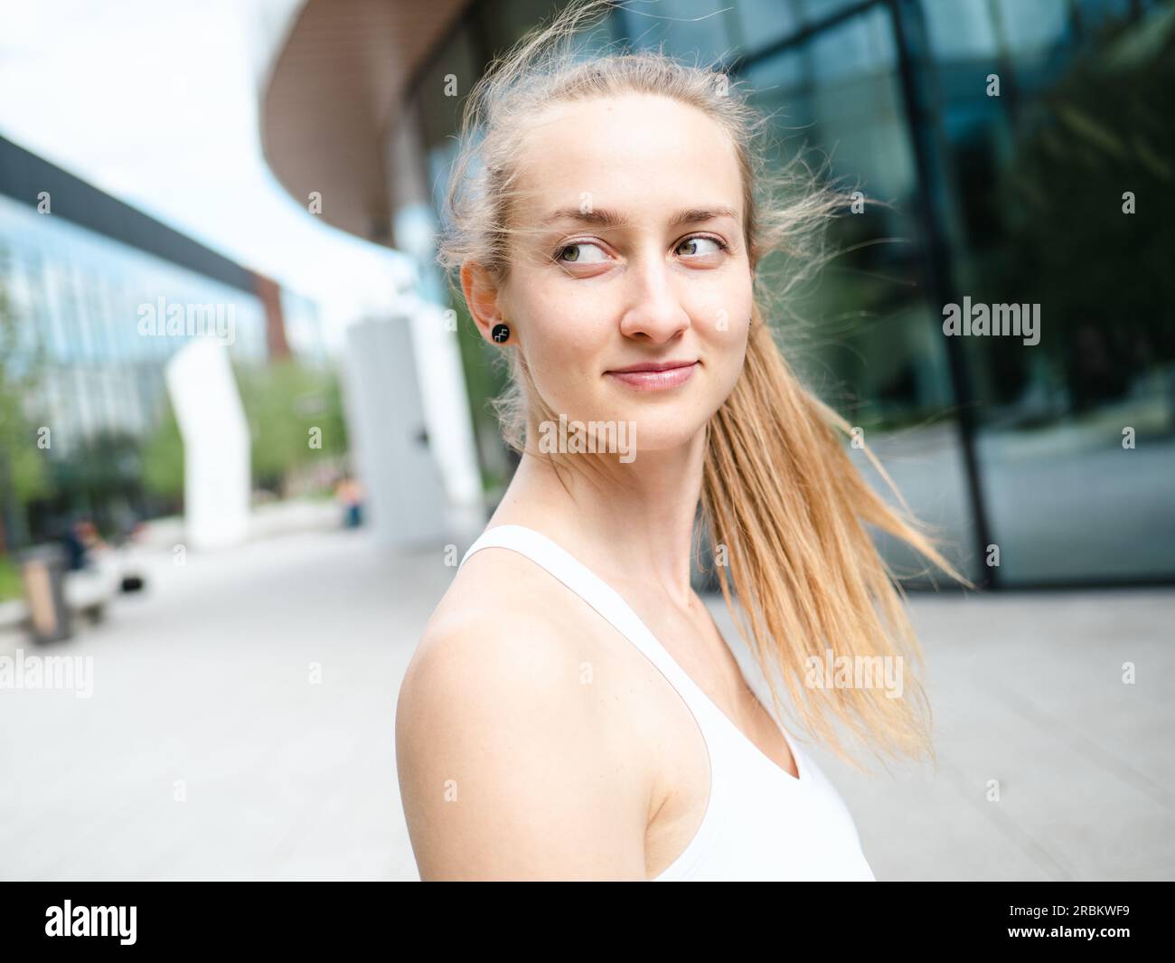 Junge blonde Frau im Freien an sonnigen Sommertagen mit urbanem Hintergrund, aussehende Seite Stockfoto