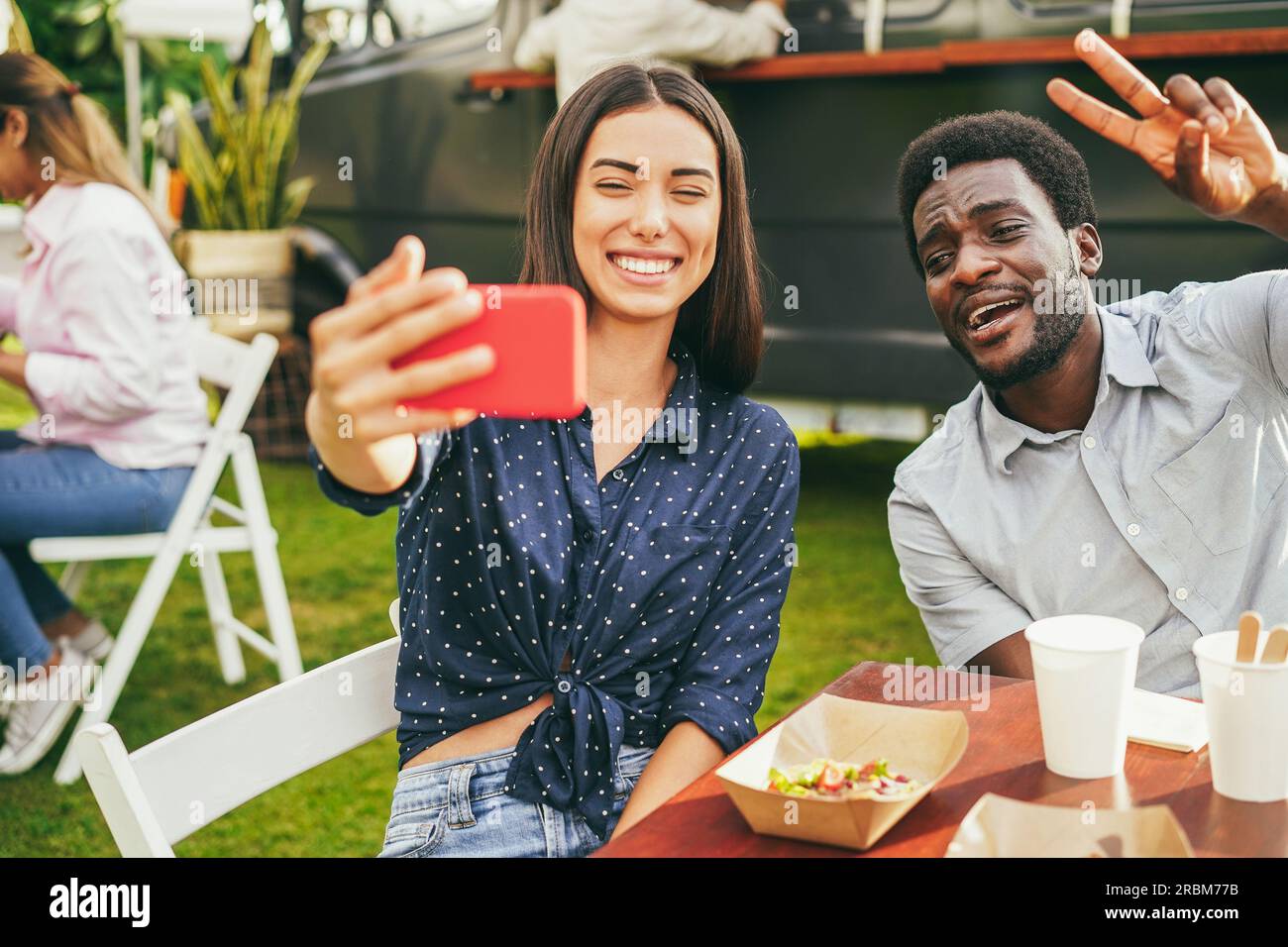 Multirassische Menschen, die Spaß haben, Selfie mit dem Mobiltelefon im Food Truck Restaurant im Freien zu machen - Fokus auf afrikanisches Männergesicht Stockfoto
