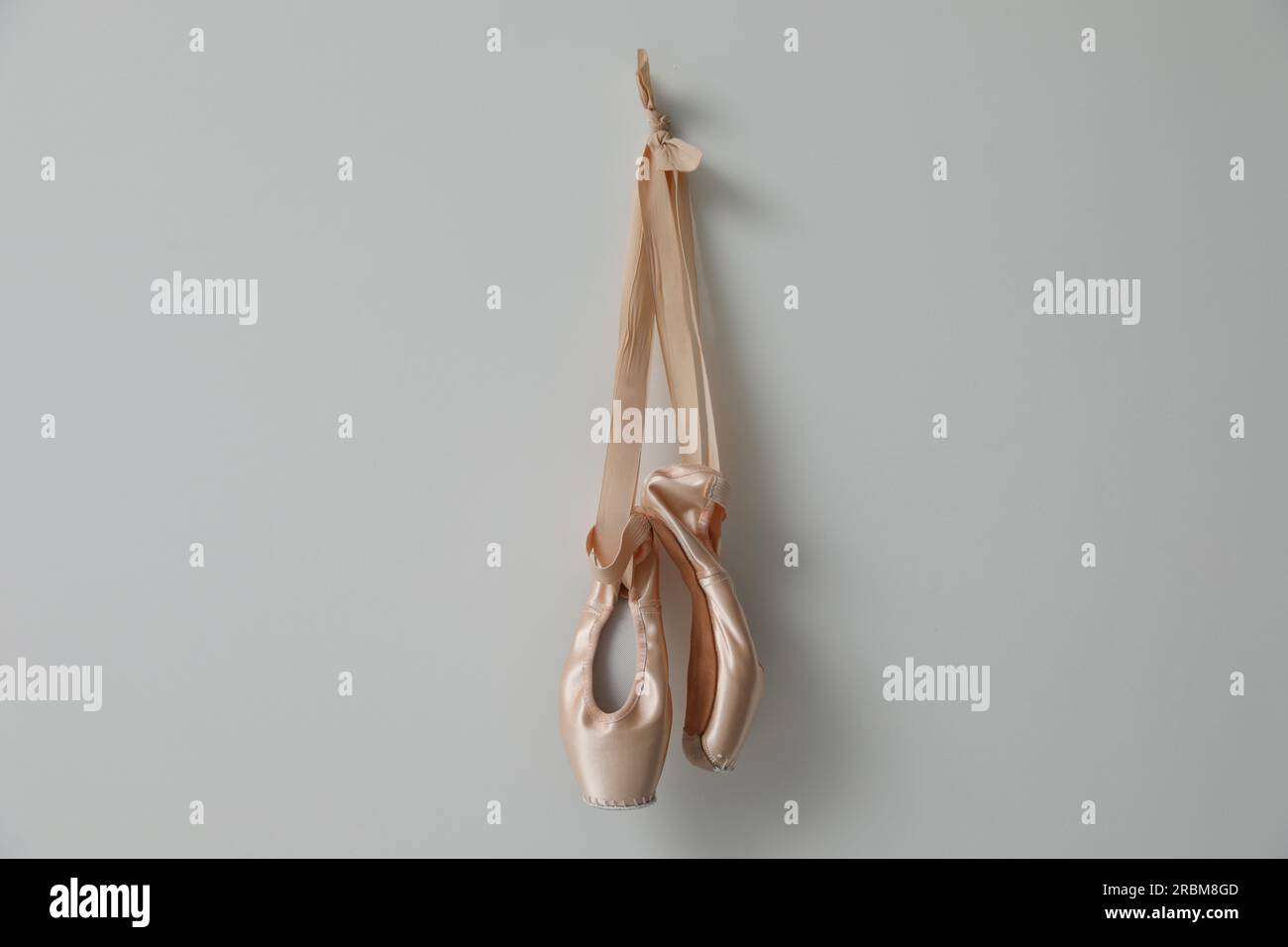 Wunderschöne beige Ballettschuhe mit niedlichen Bändern, die an hellgrauen Wänden hängen Stockfoto