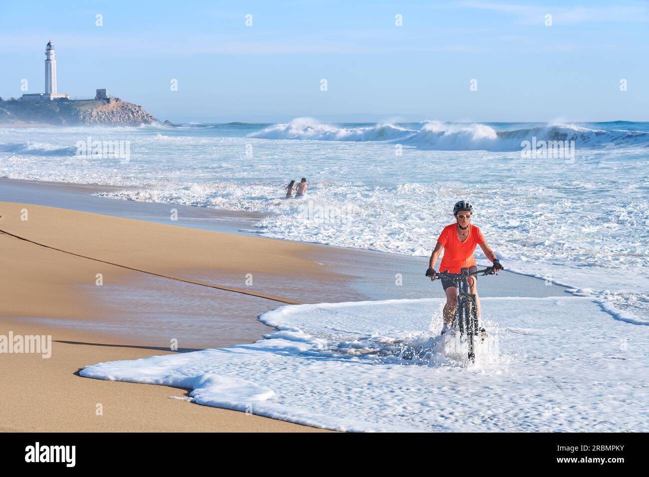 Aktive Frau, die ihr elektrisches Mountainbike am Strand von Cape Trafalgar, Costa de la Luz, Andalusien, Spanien, fährt Stockfoto