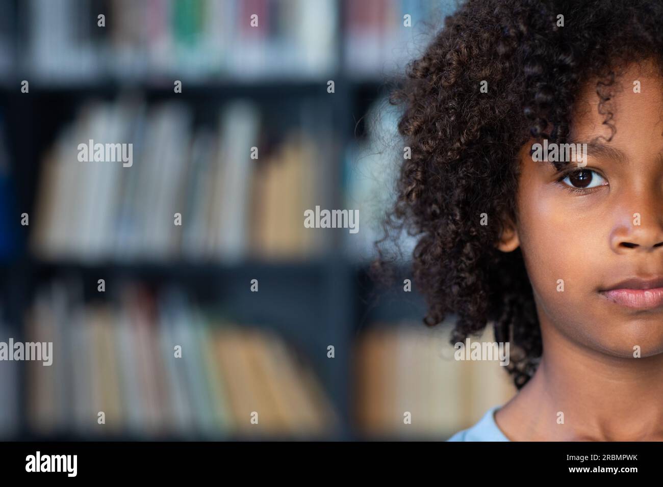 Halbgesichtsporträt eines afroamerikanischen Schuljungen mit Afrohaar in einer Bibliothek mit Kopierraum. Bildung, Kindheit, Inklusivität, Grundschule und l Stockfoto