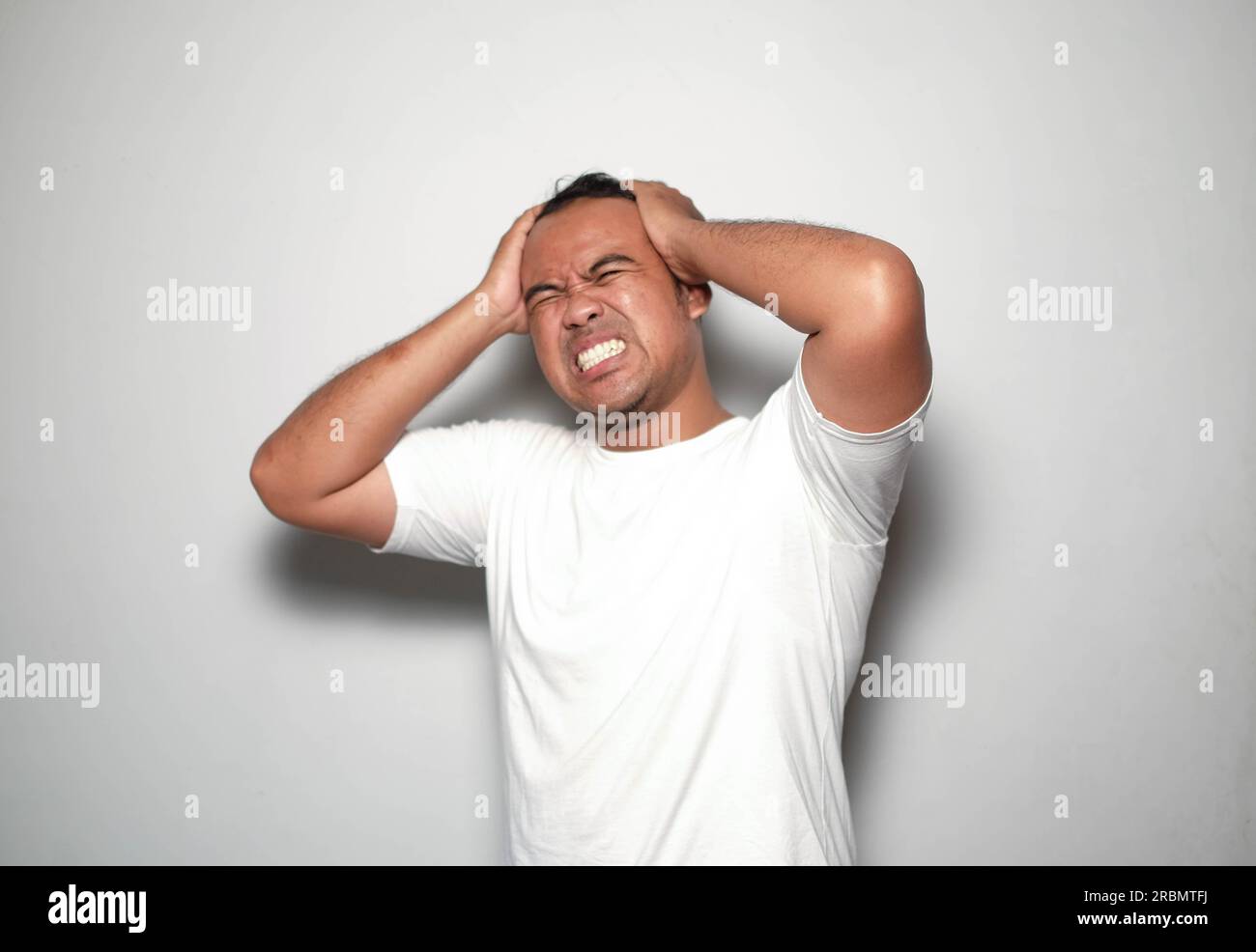 Ein Foto von einem Asiaten, der gestresste zwei Hände hat, die einen Stresskopf halten und ein weißes T-Shirt tragen, isoliert von weißem Hintergrund. Sieht deprimiert aus Stockfoto