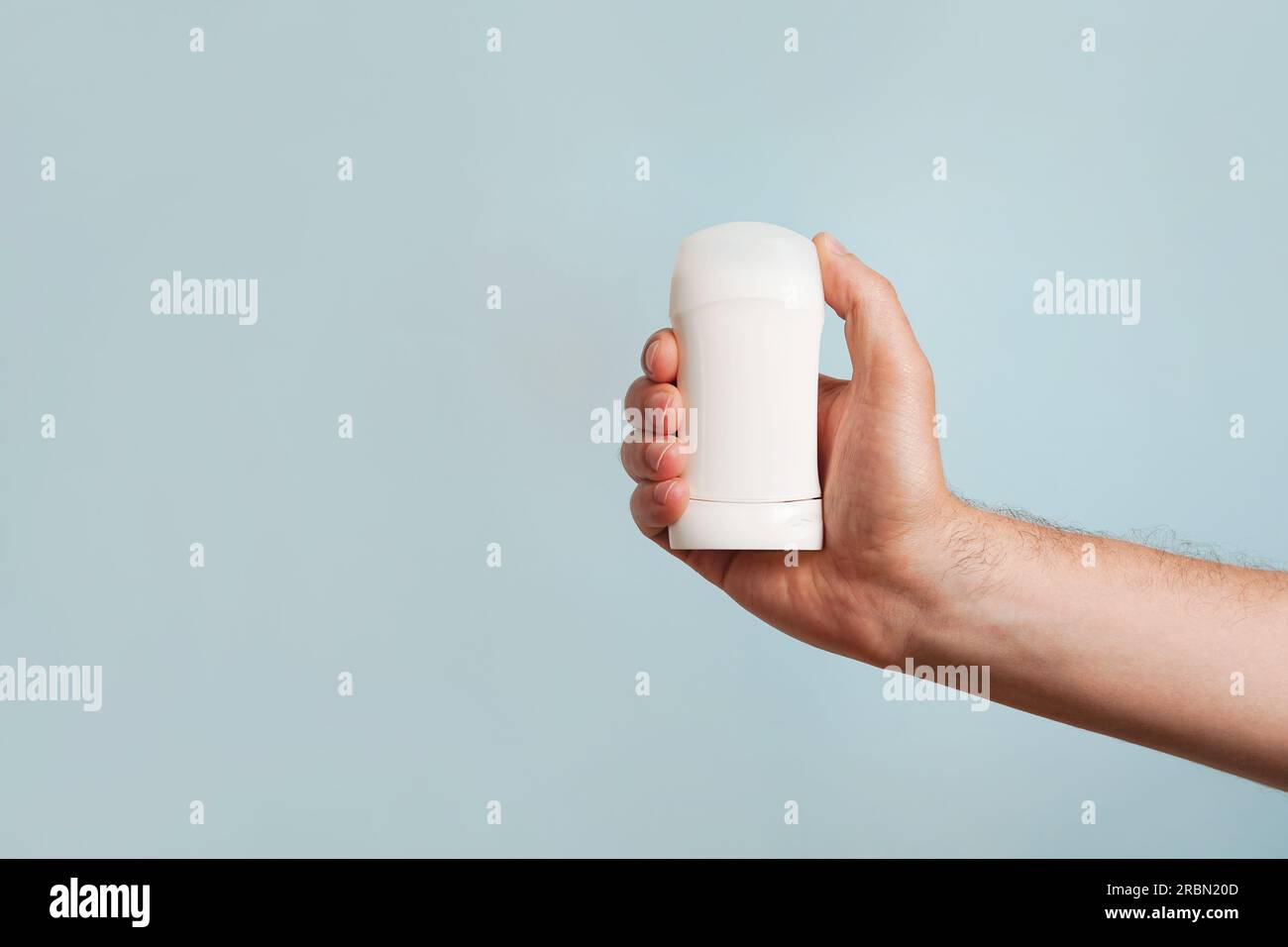Männliche Hand hält weißes Deodorant auf blauem Hintergrund. Nahaufnahme. Speicherplatz kopieren Stockfoto