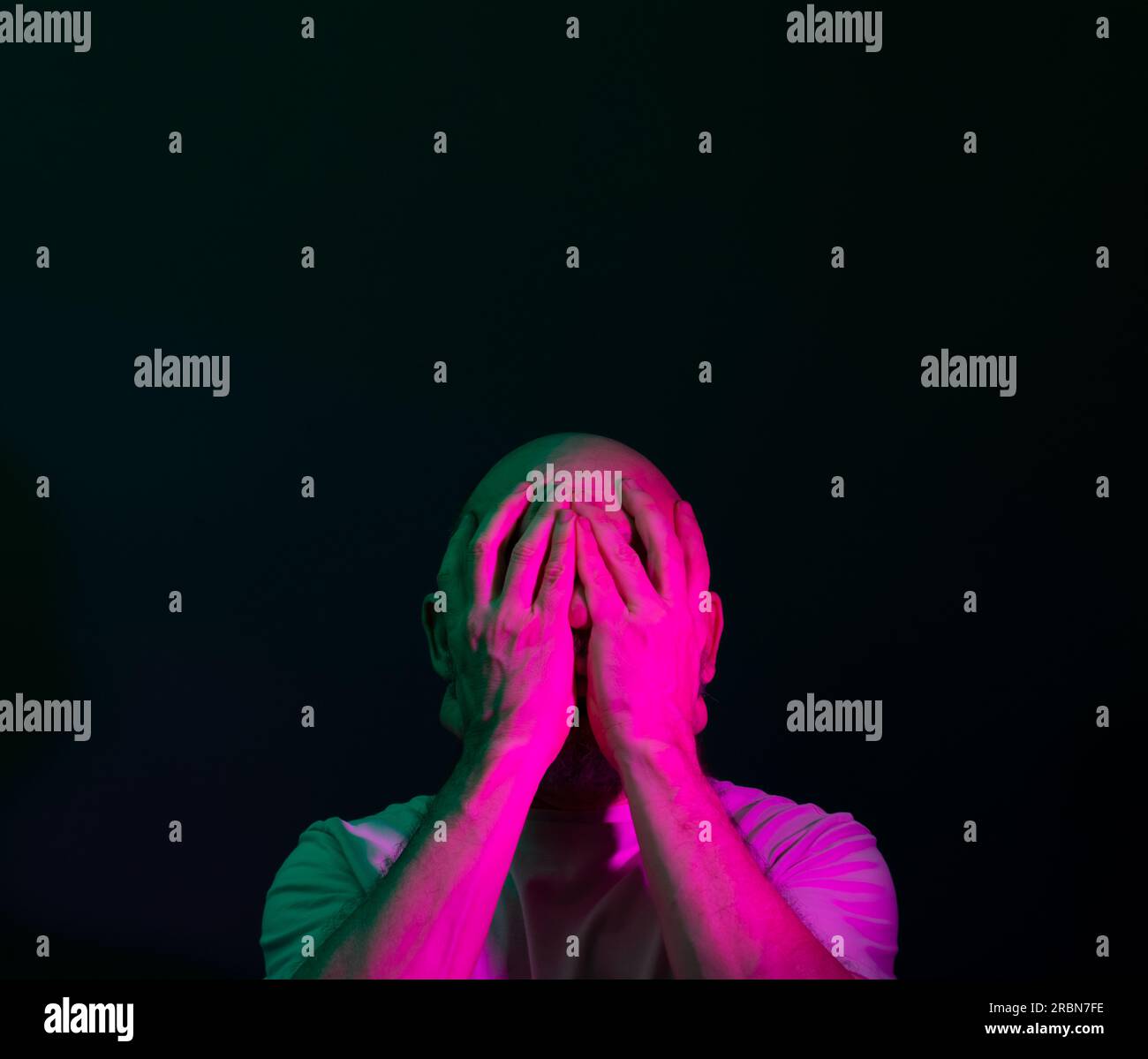 Ein Mann in seinen 50s, emotional erschüttert, der Stress oder Schmerz zeigt. Schwächegefühl oder Depression. Isoliert auf dunklem Hintergrund. Stockfoto