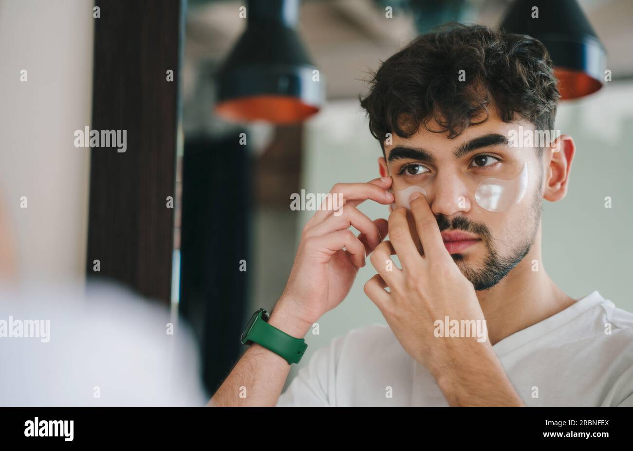 Junger bärtiger Mann in lässiger Kleidung, der morgens beim Blick in den Spiegel Pflaster aufklebt. Stockfoto
