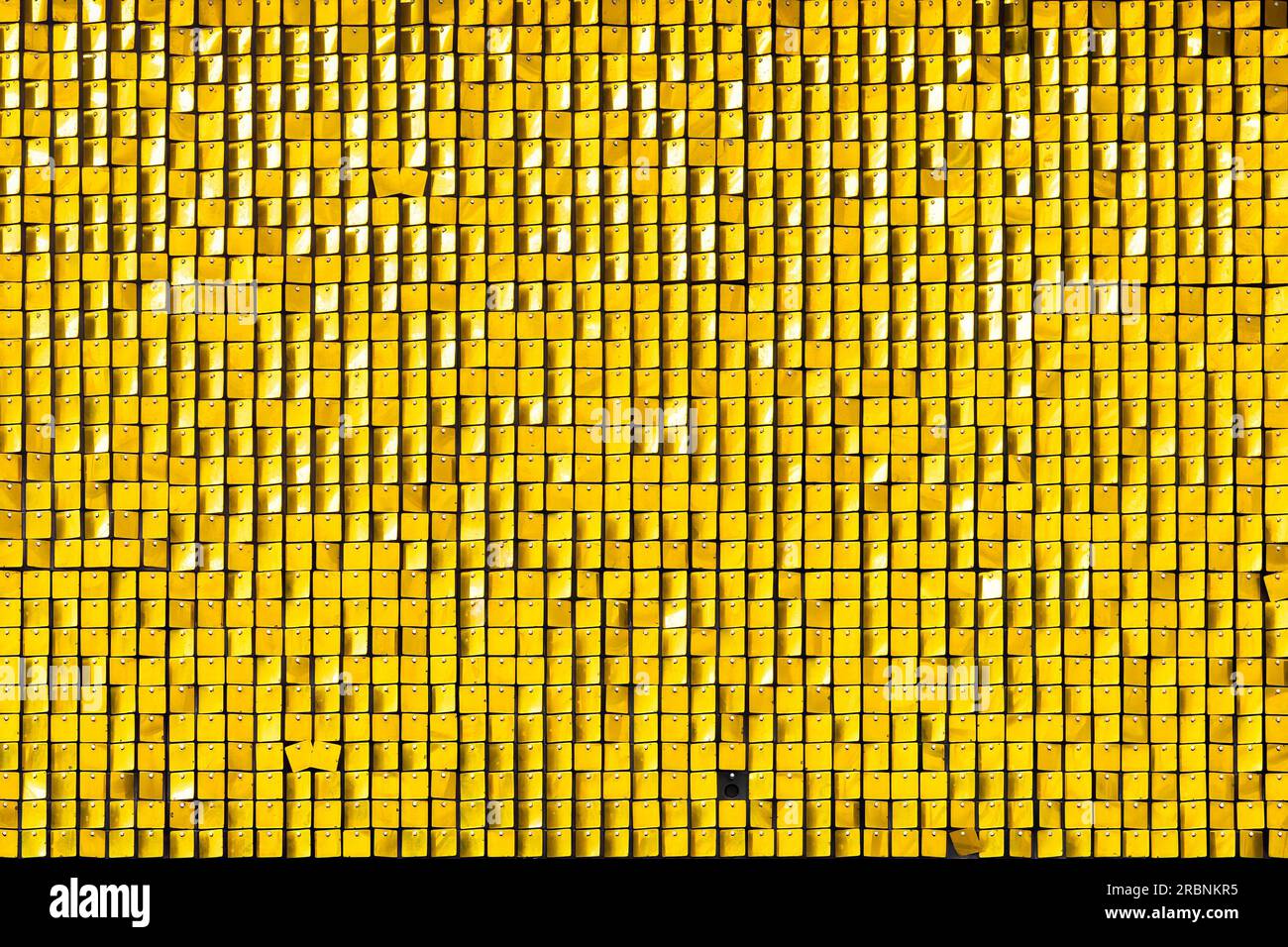 Ein Display aus kleinen gelben Quadraten aus Kunststoff und einer Gruppe nahe beieinander. Die Quadrate schimmern im Sonnenlicht, während eine Brise sie sanft bewegt Stockfoto