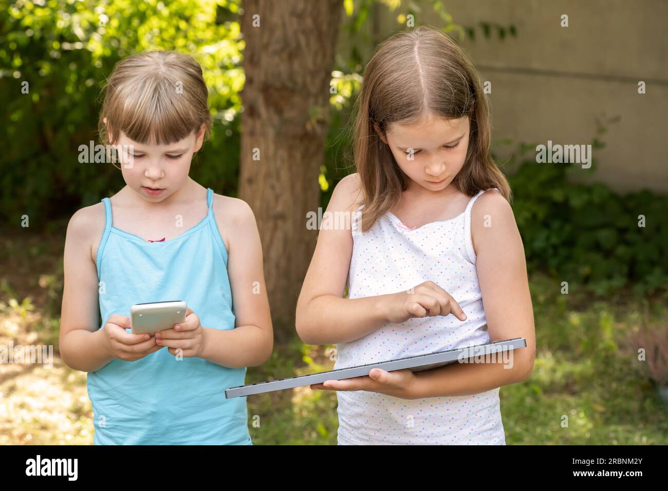 Zwei Mädchen im Grundschulalter halten, benutzen elektronische Geräte, einen Taschenrechner und eine Tastatur. Werbekonzept für Kinder und Elektronik, Außenaufnahme. Zwei Pups Stockfoto