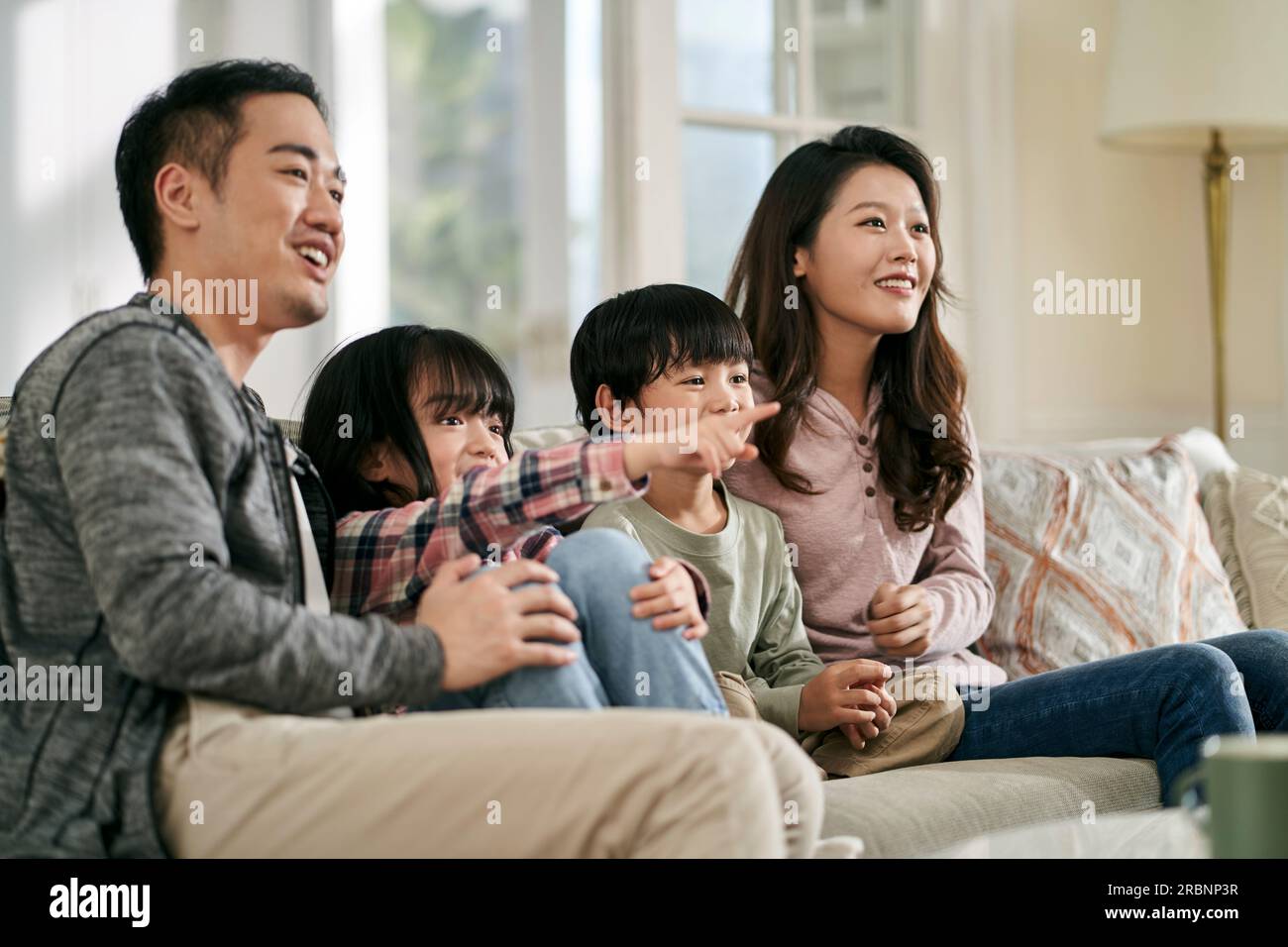 Glückliche asiatische Familie mit zwei Kindern, die zu Hause auf der Couch sitzen und zusammen fernsehen Stockfoto