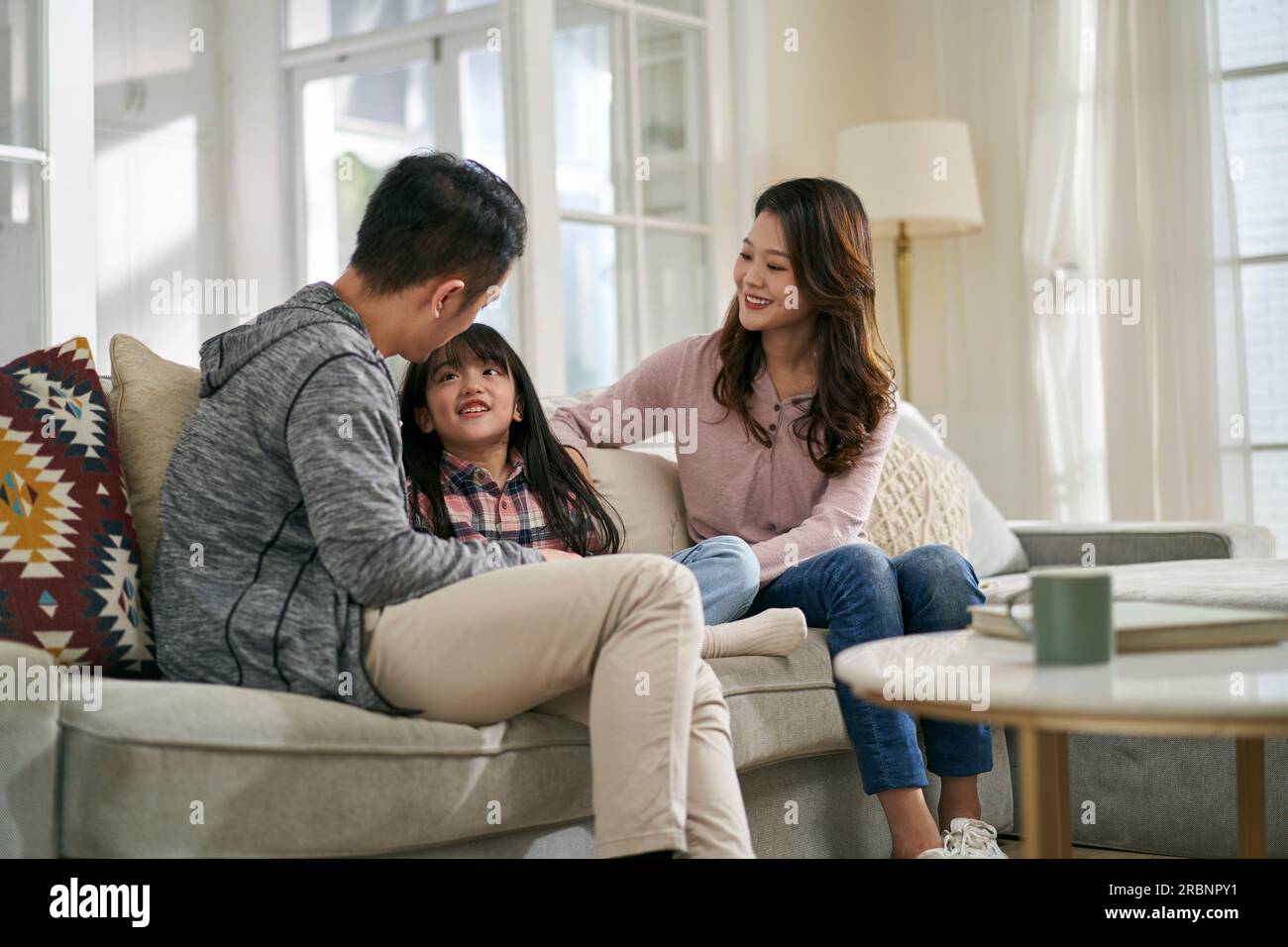 Junge asiatische Mutter und Vater, die zu Hause auf dem Familientisch sitzen und ein angenehmes Gespräch mit ihrer Tochter führen Stockfoto