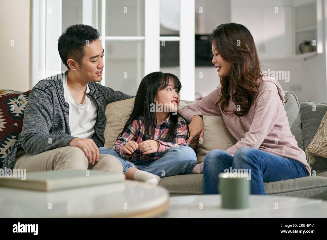 Junge asiatische Mutter und Vater, die zu Hause auf dem Familientisch sitzen und ein angenehmes Gespräch mit ihrer Tochter führen Stockfoto