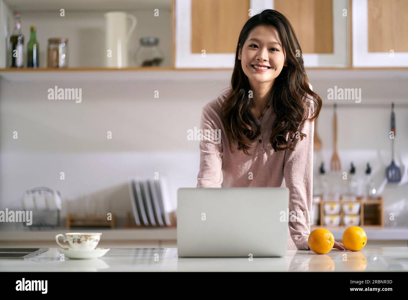 Portrait einer glücklichen, erfolgreichen Frau, Freiberuflerin, die hinter einer Küchentheke zu Hause steht und die Kamera lächelt Stockfoto