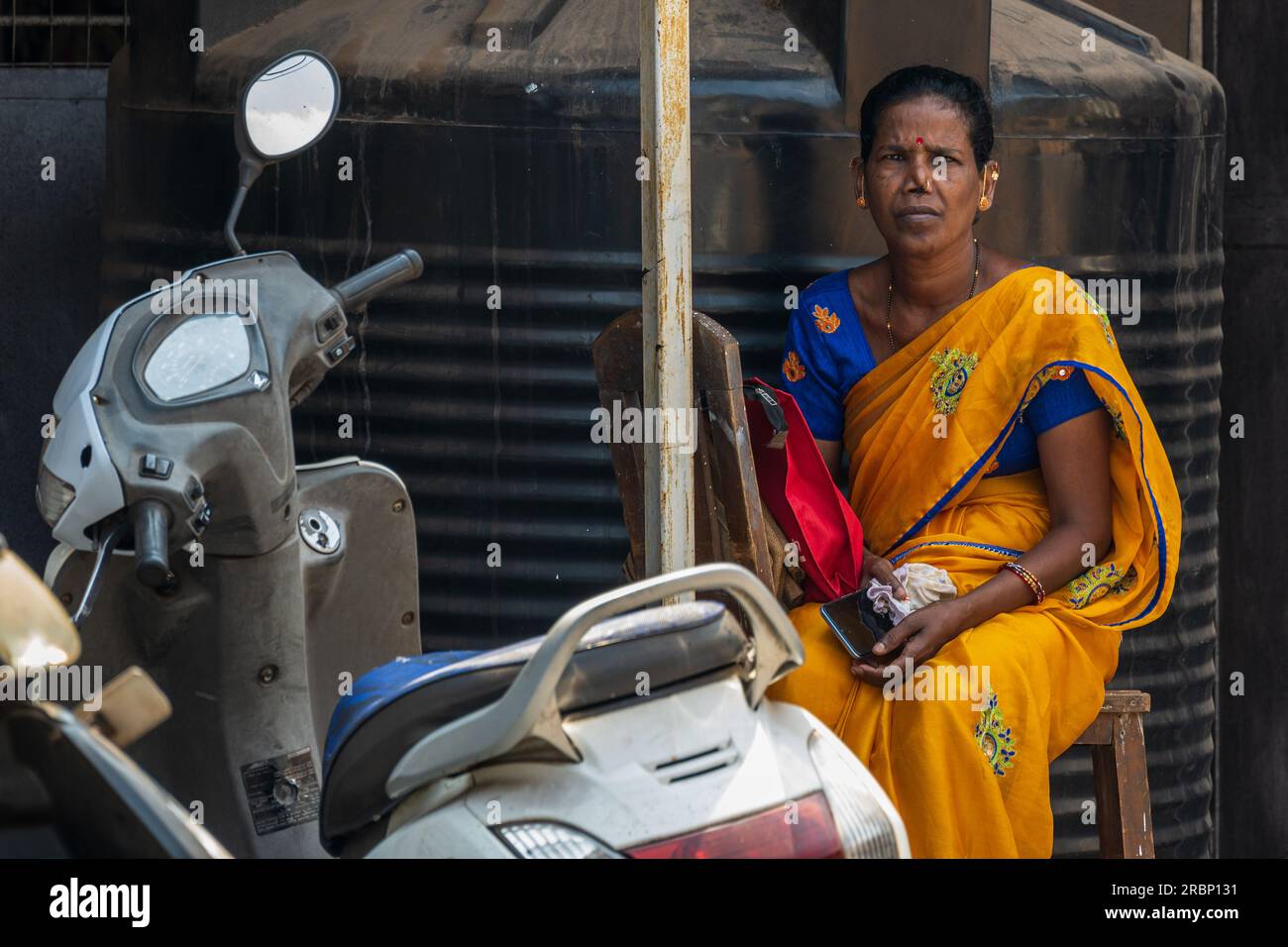 Goa, Indien -- 10. April 2023. Eine indische Frau in Goa, die eine Saree trägt, sitzt still und beobachtet die Szene vor ihr. Stockfoto