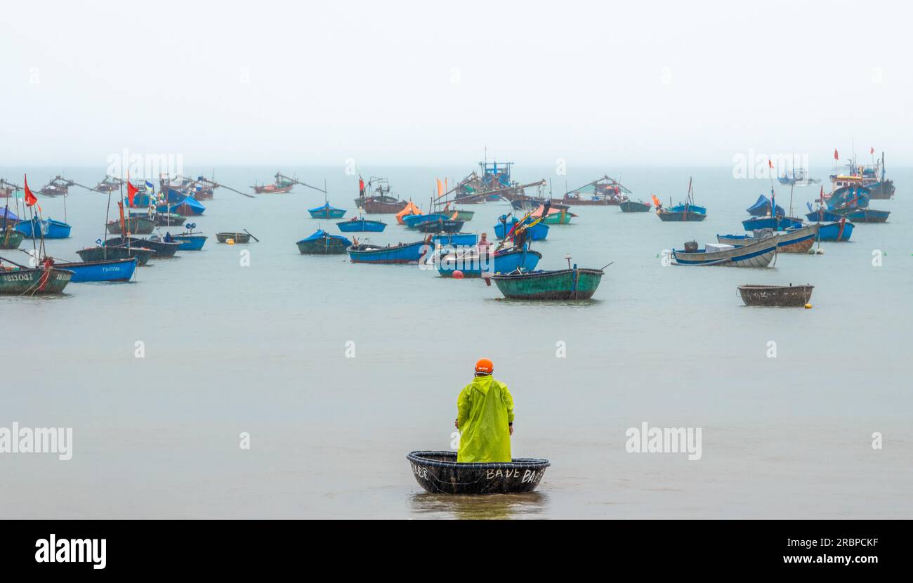 Ein vietnamesischer Fischer steht im Regen, während er sein Korakel zu seinem Fischerboot in Danang, Vietnam, führt. Stockfoto