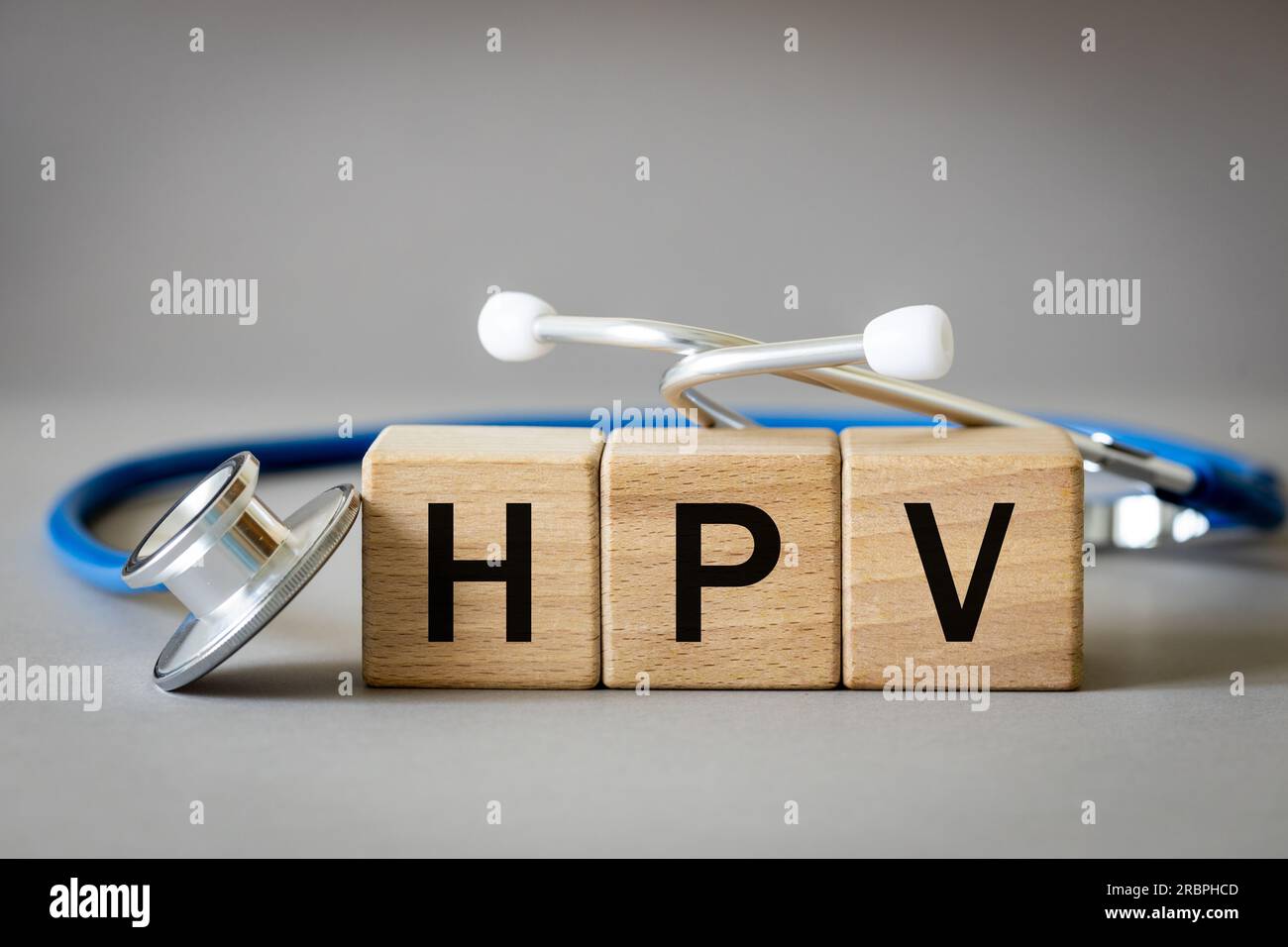 Der Arzt sorgte das Wort HPV aus Holzblöcken, humanem Papillomavirus, medizinischem und Gesundheitskonzept, medizinischem Stethoskop und grauem Hintergrund Stockfoto