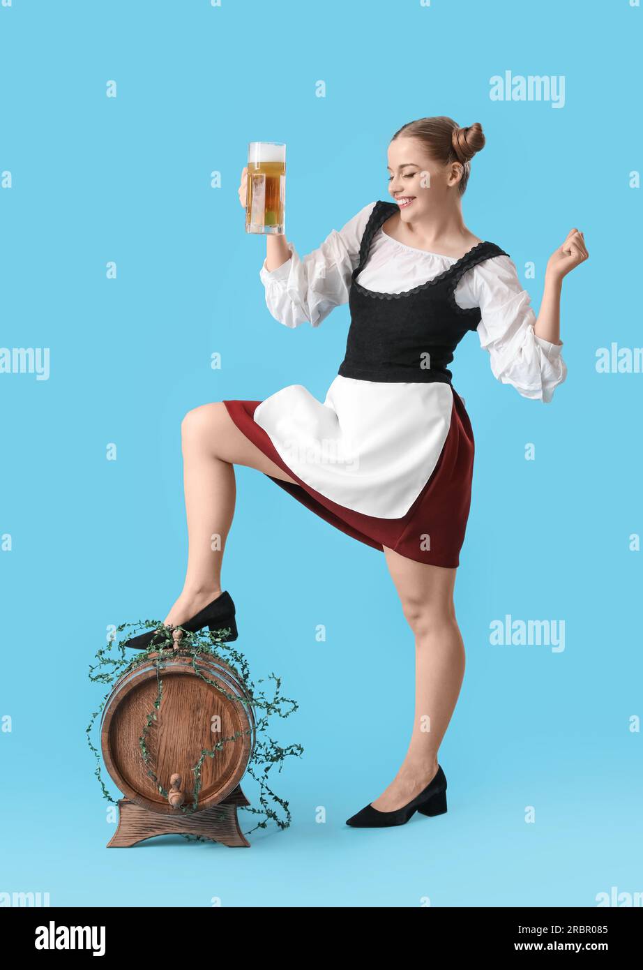 Wunderschöne Oktoberfest-Kellnerin mit Bier und Fass auf blauem Hintergrund Stockfoto