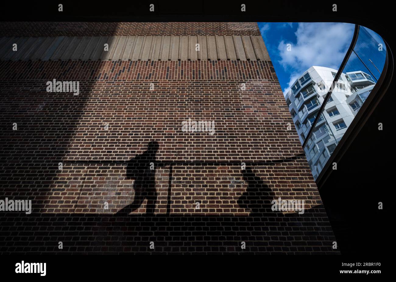 Battersea, London, Großbritannien: Schatten auf einer Ziegelmauer, die Menschen auf einem Gehweg über dem Kopf zeigen. Gesehen am umgebauten Kraftwerk Battersea. Stockfoto