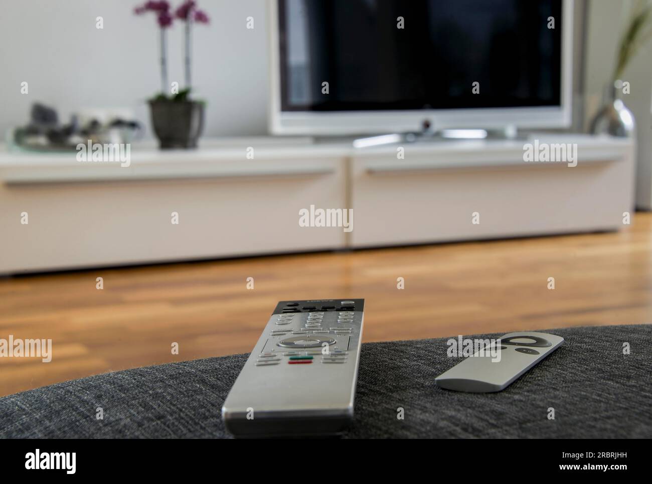 Eine Fernbedienung liegt auf dem grauen Sofa, und das Home Entertainment-System befindet sich im Hintergrund Stockfoto