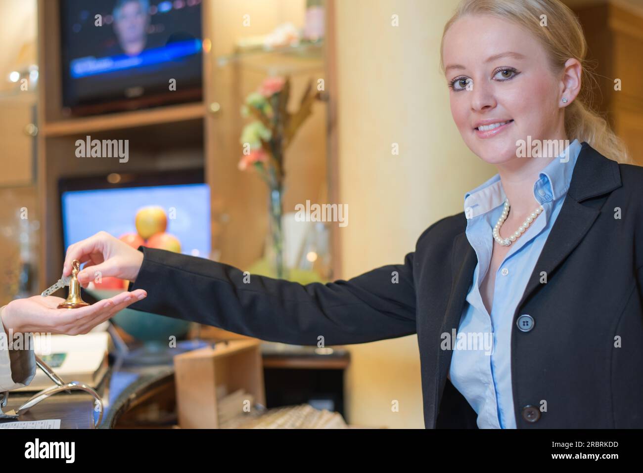 Lächelnde junge weibliche Rezeptionistin in einer Hotellobby, die einem weiblichen Kunden im Rahmen eines Hospitality-, Service- und Tourismuskonzepts die Zimmerschlüssel übergibt Stockfoto