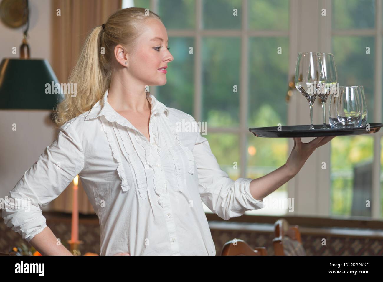 Elegante, wunderschöne junge Frau serviert Getränke anmutig und balanciert das Tablett mit Gläsern Weißwein auf ihren Fingerspitzen, die im Profil mit einem stehen Stockfoto