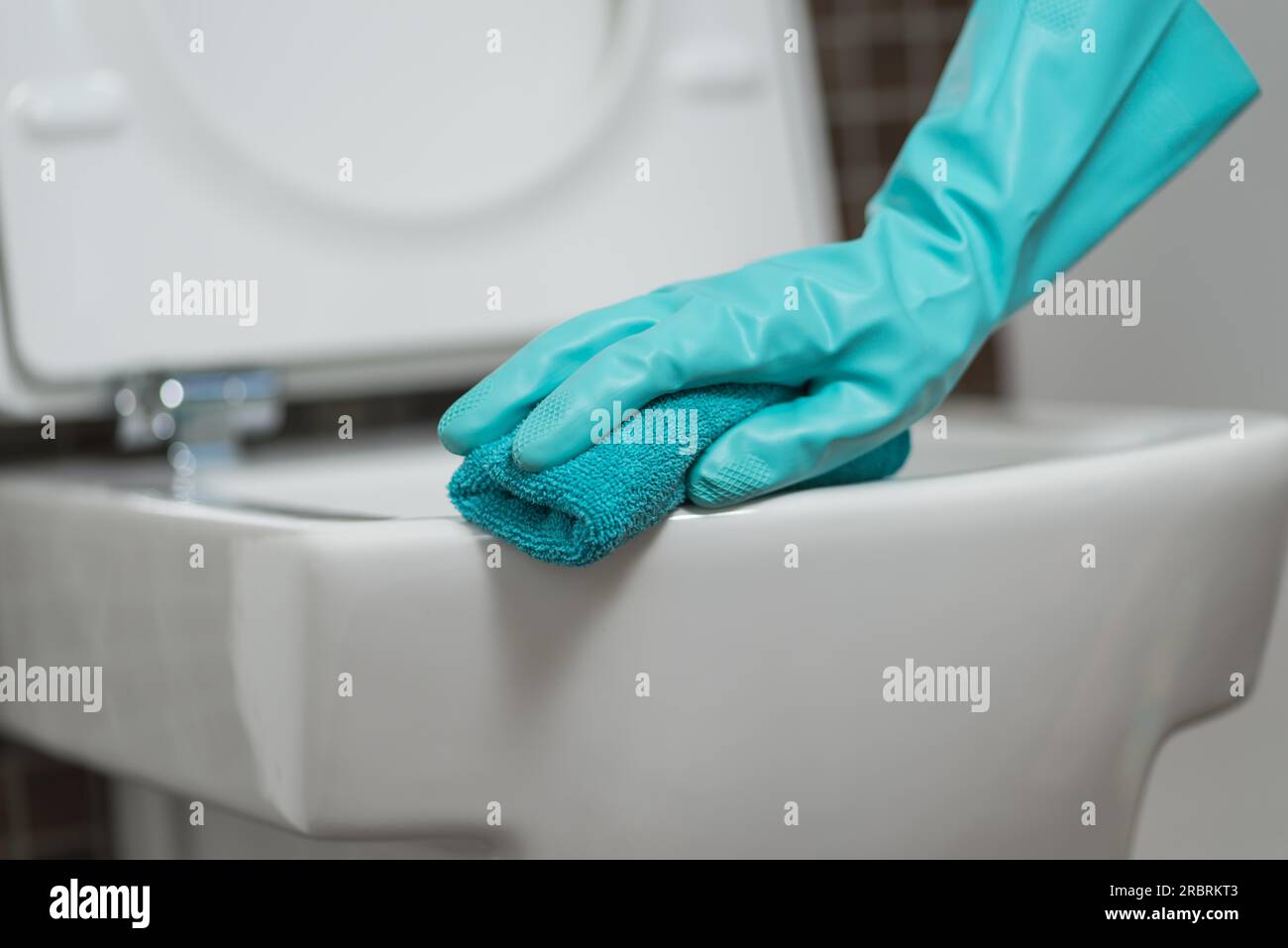 Hand einer Person, die den Toilettensitz in Gummihandschuhen mit einem Schwamm reinigt, der die Unterseite während der Haushaltsführung gegen Keime und Bakterien desinfiziert Stockfoto