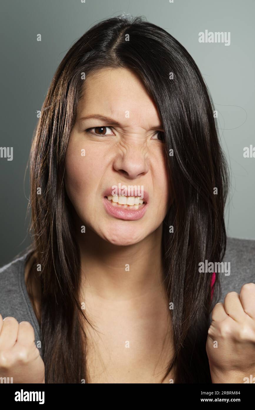 Nahaufnahme einer attraktiven jungen Frau mit einem entsetzlichen Gesichtsausdruck, die ihre Hände in Frustration und Verzweiflung zusammenhält, während sie mit geballten Zähnen anstarrt Stockfoto