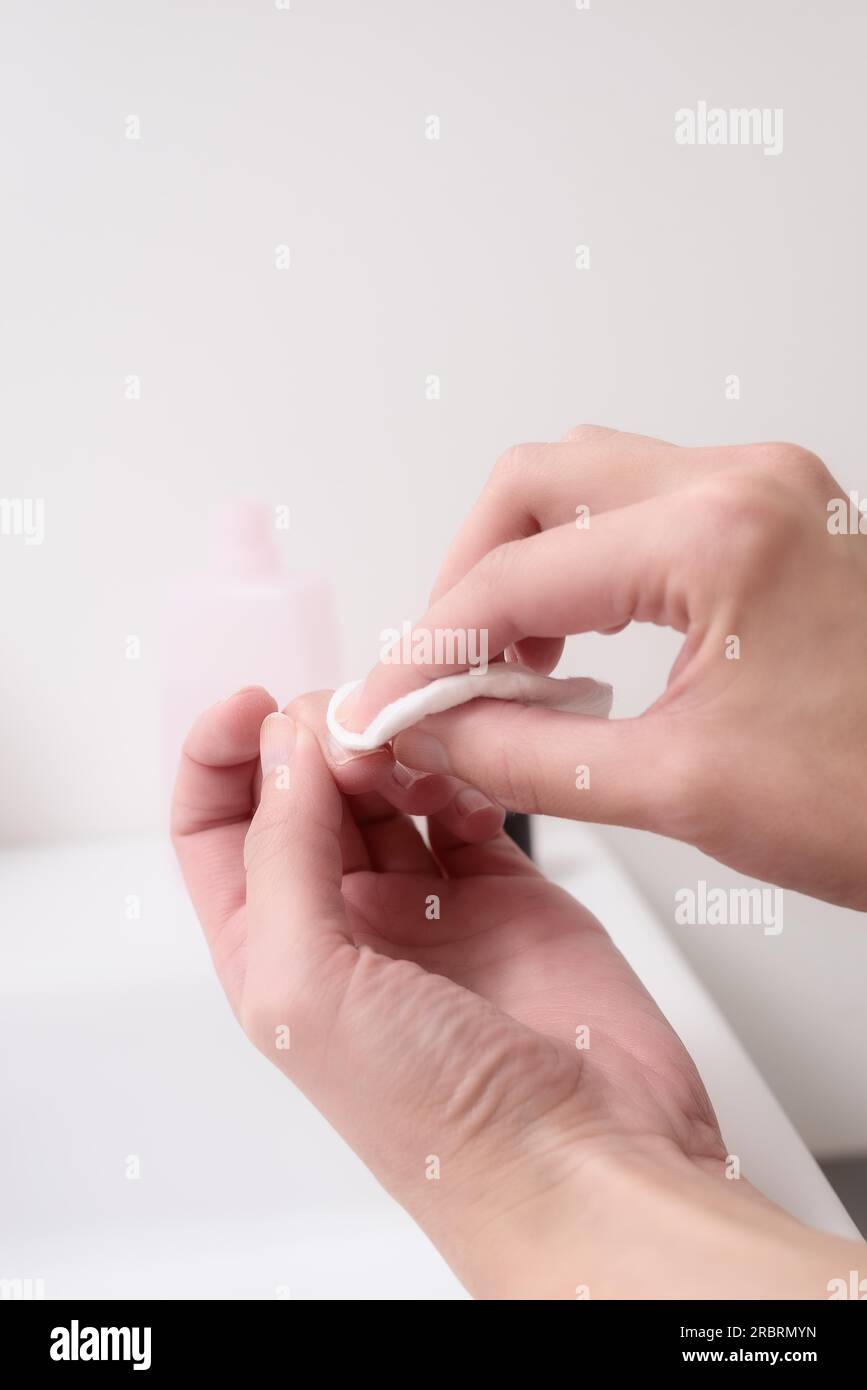 Frau entfernt Nagellack mit Aceton auf einem kleinen Wattepad am Rand eines Handbeckens, während sie sich um ihre Nägel und Nagelhäute in einem gesunden und Stockfoto