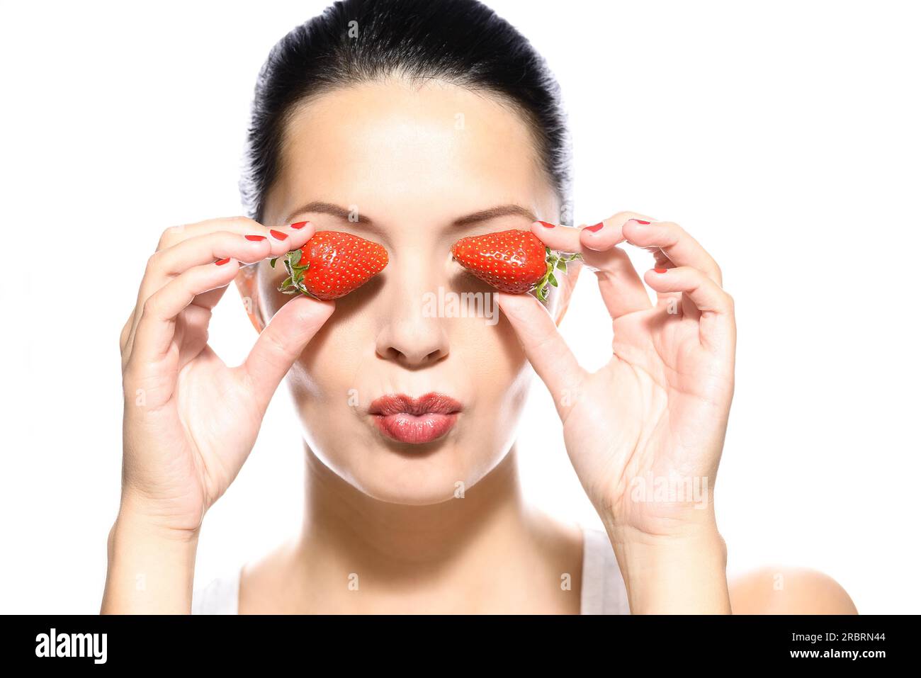 Schöne junge Frau mit einem schönen warmen Lächeln und gesunde gebräunte Haut hält zwei Reife rote Erdbeeren an den Seiten ihrer Augen, isoliert auf weiss Stockfoto