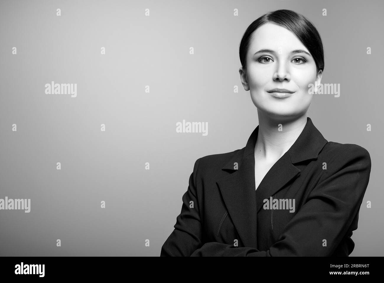 Schwarz-weißes Porträt einer wunderschönen, eleganten, professionellen Frau, die mit gefalteten Armen in einer stilvollen Jacke auf die Kamera blickt, mit einem Stockfoto