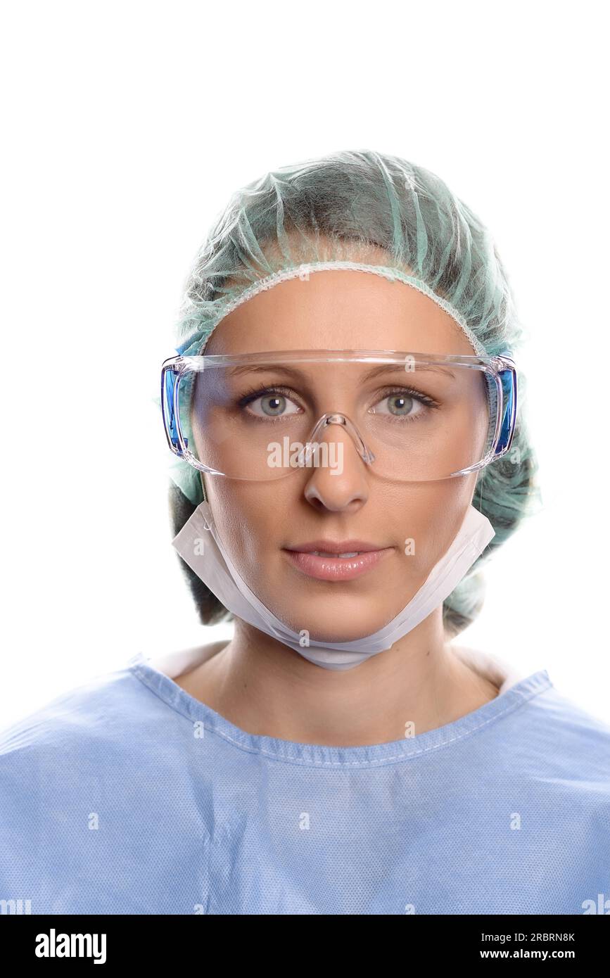 Junge Krankenschwester oder Ärztin in OP-OP-Kittel, Maske, Schutzbrille und eine Kappe, die direkt auf Kamera, Kopf und Schultern blickt Stockfoto