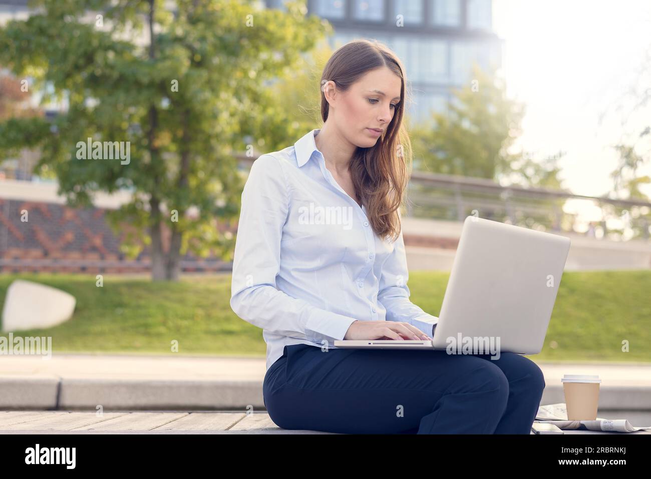 Attraktive junge Frau trägt formelle Kleidung während der Arbeit im Freien auf einem Laptop, mit einer drahtlosen Verbindung mit dem Internet, das in einer Schönen Tag des Sommers Stockfoto