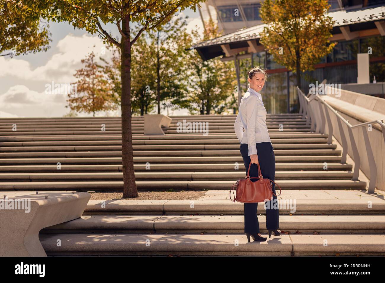 Stilvolle Frau in Hosen tragen einer Handtasche klettern einen Flug von konkreten Outdoor urban Treppen anhalten zu drehen und zur Seite schauen Stockfoto