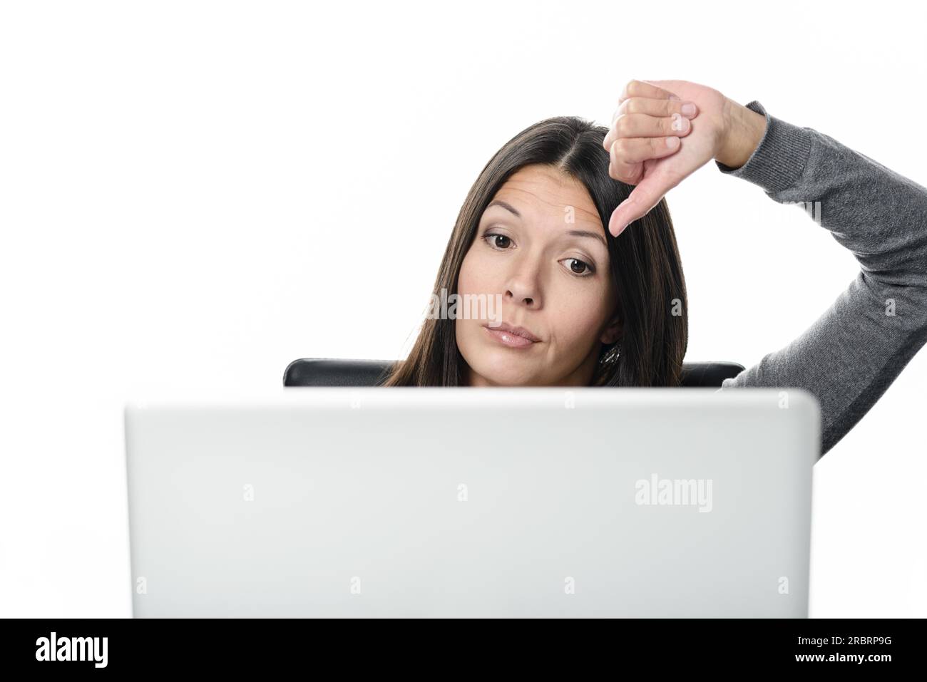 Unzufriedene junge Frau, die mit einem Laptop arbeitet und ein Schild mit Daumen zeigt. Isoliert auf weißem Hintergrund Stockfoto