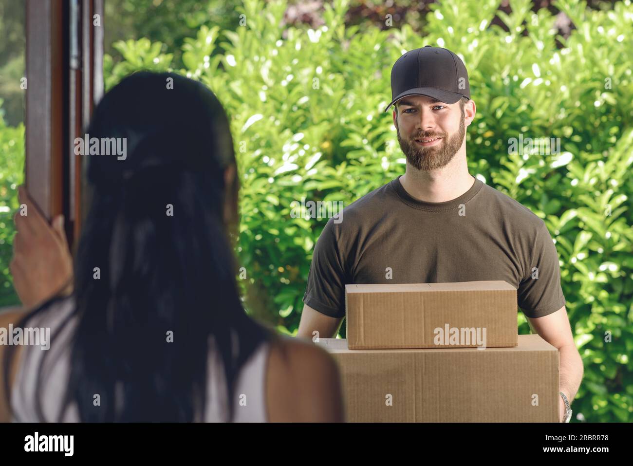 Frau beantworten die Tür zu einem attraktiven Bärtigen deliveryman zwei Kartons für Lieferung, Blick über die Schulter von hinten Stockfoto