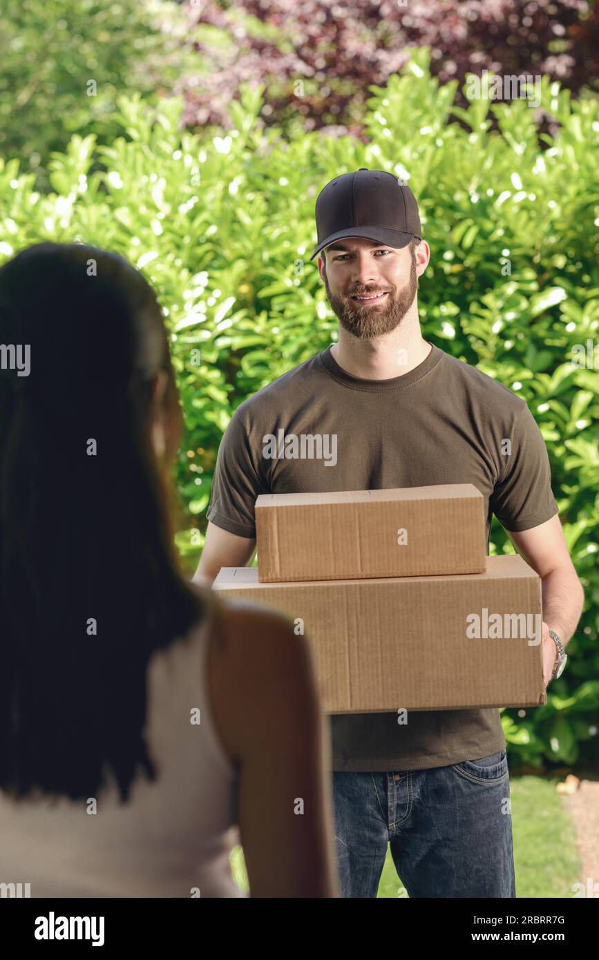 Frau beantworten die Tür zu einem attraktiven Bärtigen deliveryman zwei Kartons für Lieferung, Blick über die Schulter von hinten Stockfoto