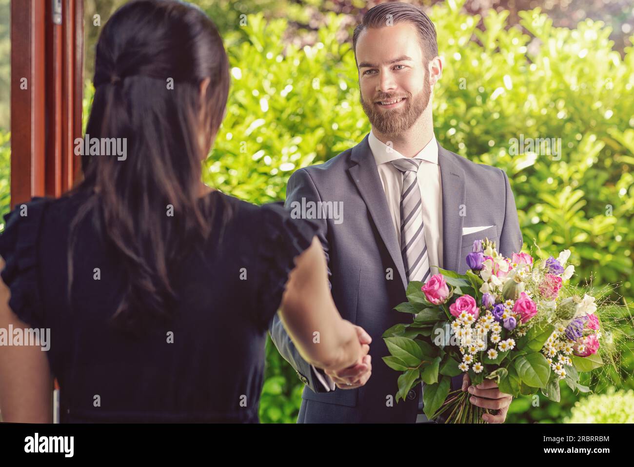 Der gutaussehende Bärtige gibt seiner Freundin einen Strauß frischer Blumen mit Happy Facial Expression Stockfoto