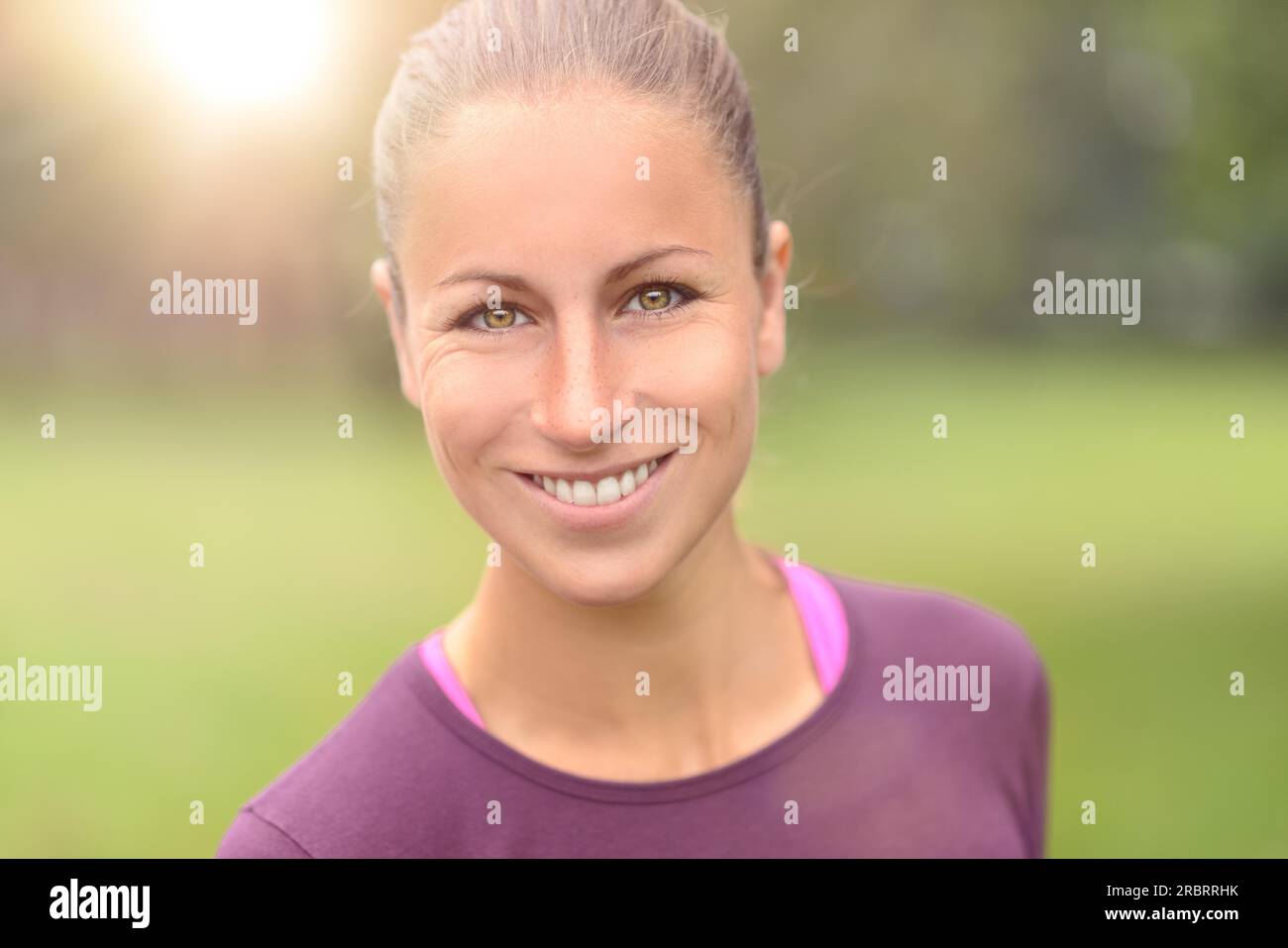 Nahaufnahme Kopf und Schulter Aufnahme einer fit sitzenden jungen Frau, die mit einem klitzekleinen Lächeln in die Kamera schaut Stockfoto