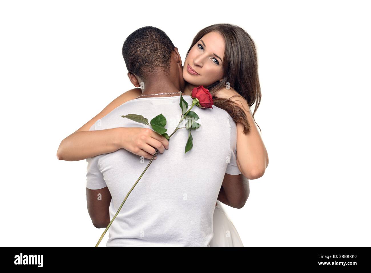 Sentimentale junge Frau umarmt ihren Freund oder Schatz, während sie sanft auf eine einzelne rote Rose lächelt, die er ihr gerade geschenkt hat, symbolisch für Liebe Stockfoto
