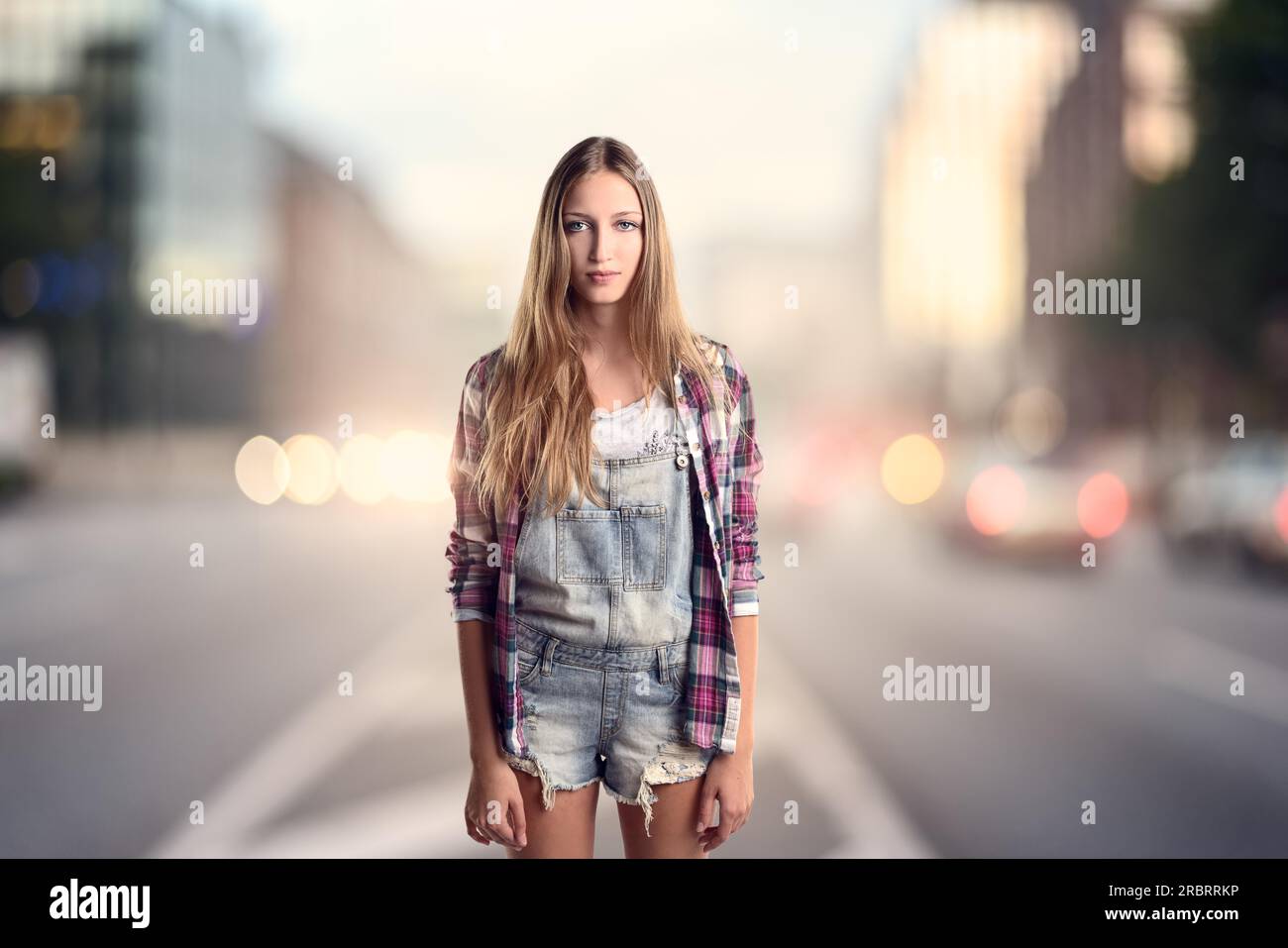 3-Viertel-Foto einer jungen blonden Frau in einem trendigen kurzen Jumpsuit-Denim mit kariertem Langarmshirt, das abends auf einer Straße steht Stockfoto