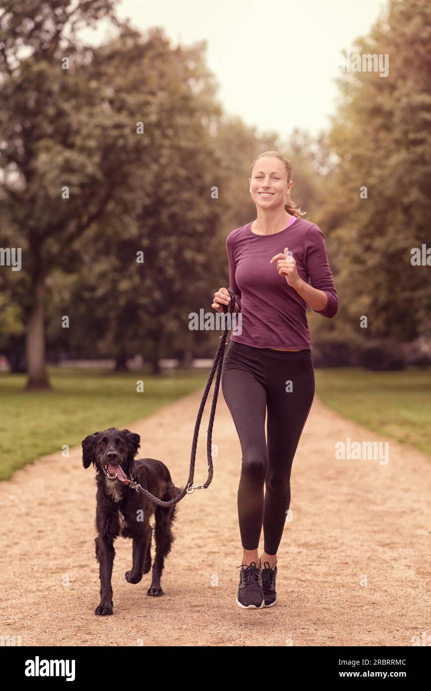 Voller Länge Schuss eine gesunde junge Frau Joggen im Park mit ihrer schwarzen Hund Stockfoto