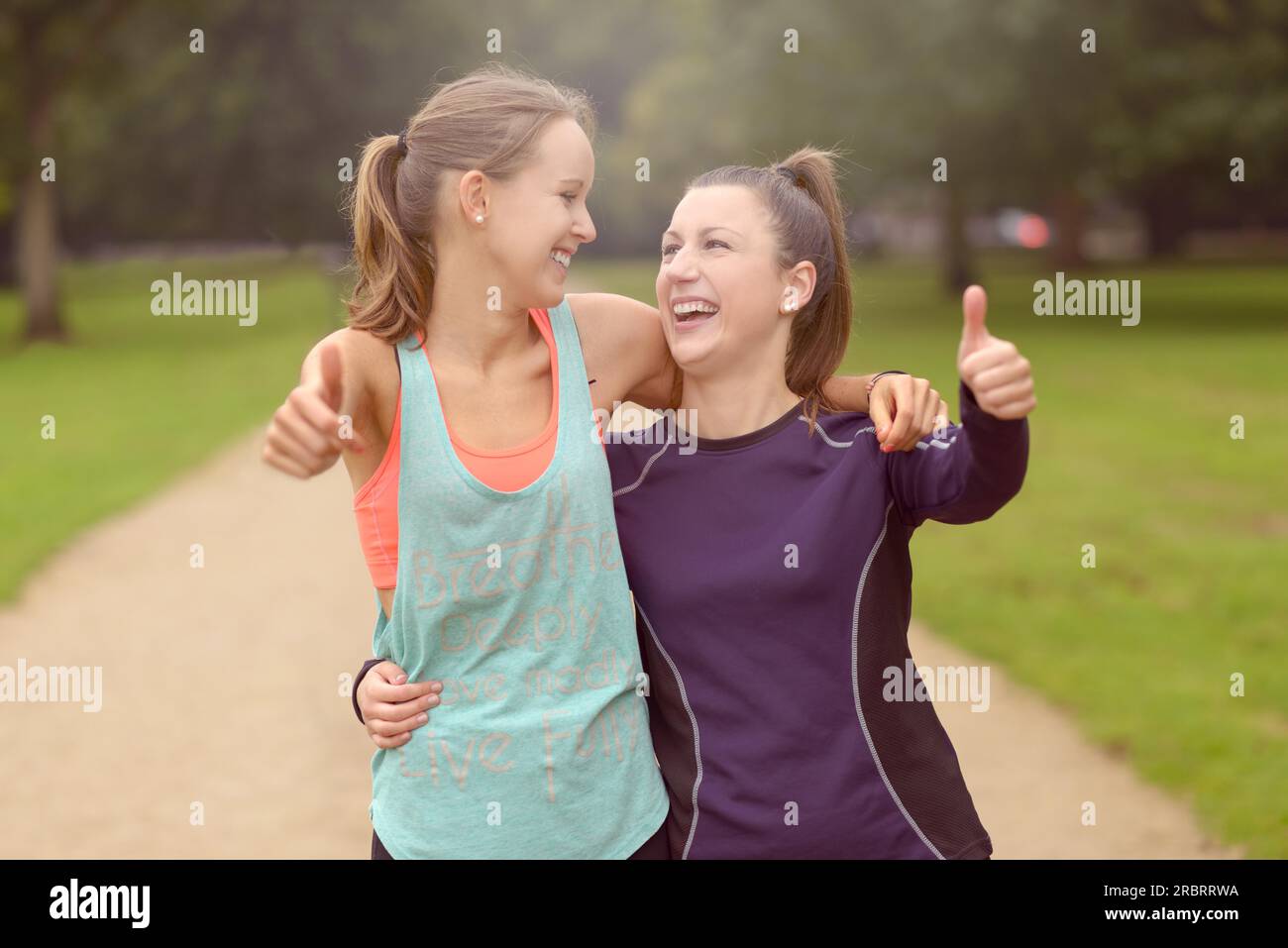 Halbkörperaufnahme von zwei glücklichen, gesunden Frauen im Park, die nach ihrem Training Daumen nach oben in die Kamera zeigen Stockfoto