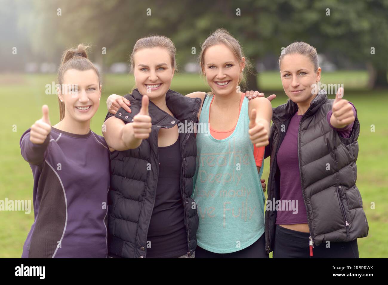 Halbkörperaufnahme von vier Athletic Women Friends, die die Daumen nach oben in die Kamera drücken, mit fröhlichen Gesichtsausdrücken Stockfoto