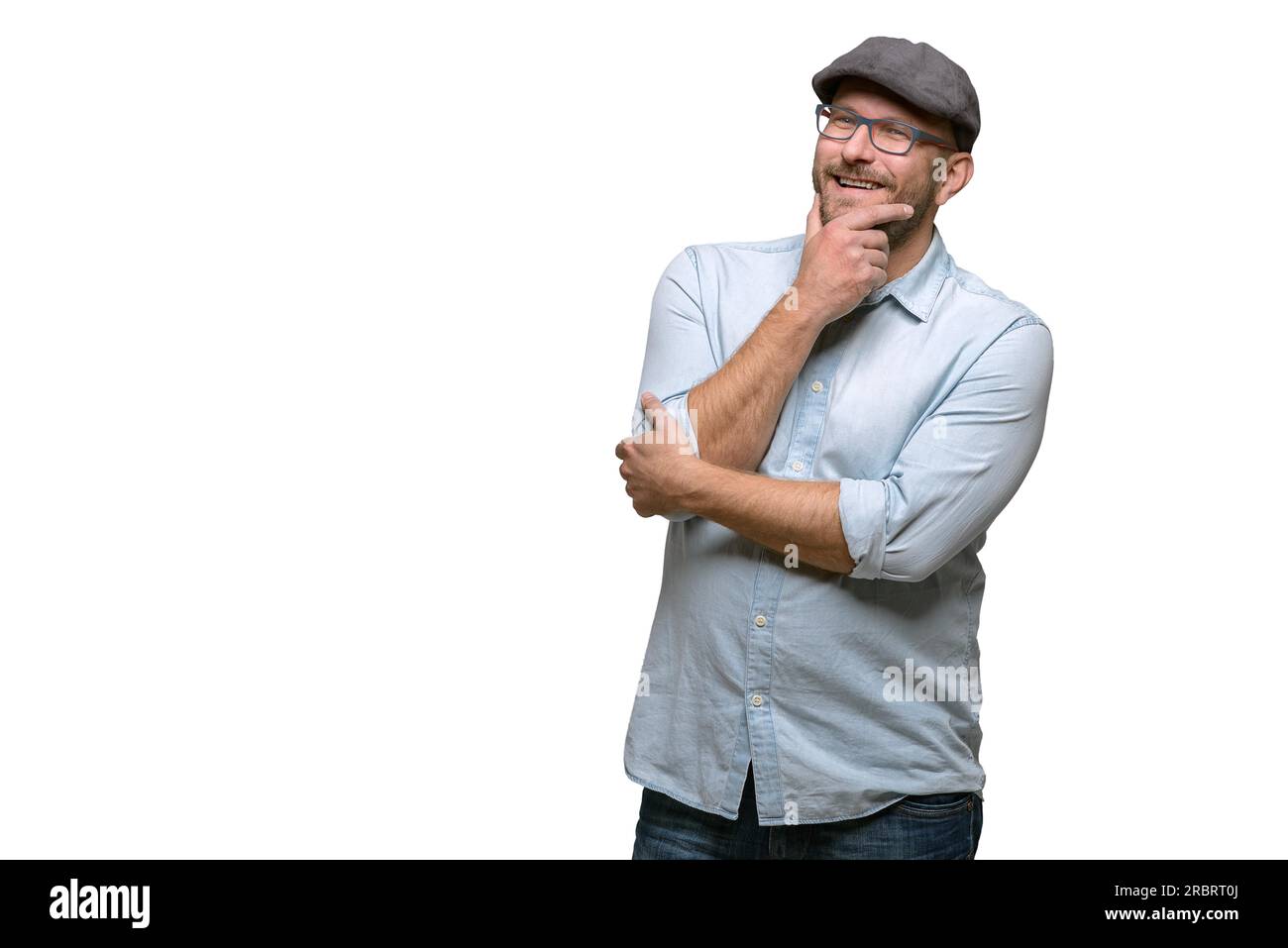 Rücksichtsvoller Mann mittleren Alters in einer Mütze und einer Brille, der mit der Hand am Kinn in die Luft starrt, mit einem nachdenklichen Ausdruck, isoliert auf Stockfoto