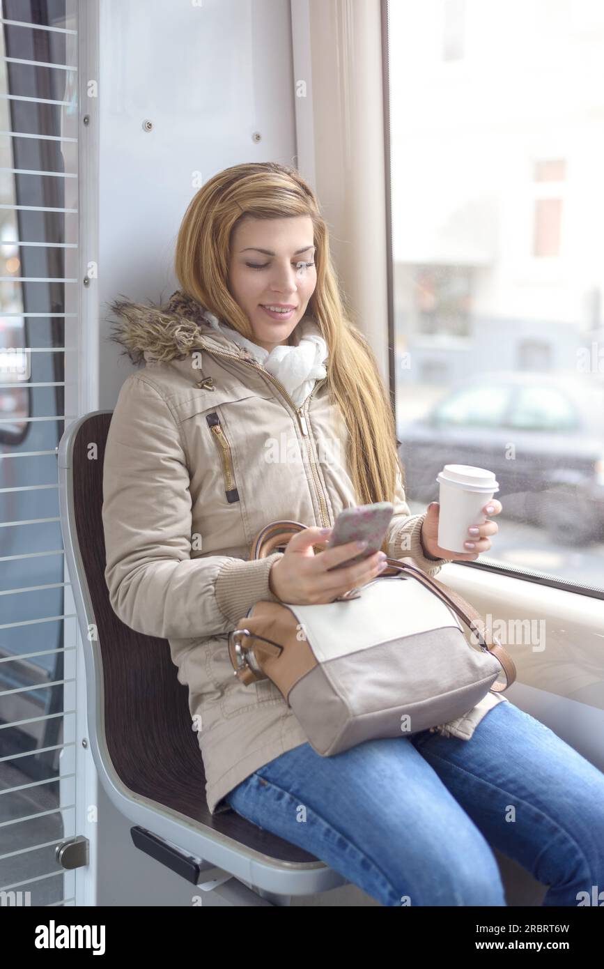 Schöne junge blonde Frau in Mantel und langen blonden Haaren sitzen auf s-Bahn-Sitz Stockfoto