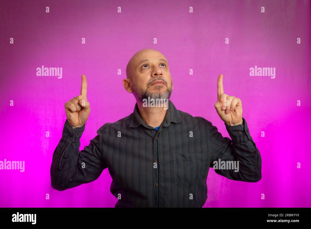 50 Jahre alter Mann, witzig, zeigt mit dem Finger nach oben. Isoliert auf pinkfarbenem Hintergrund. Stockfoto