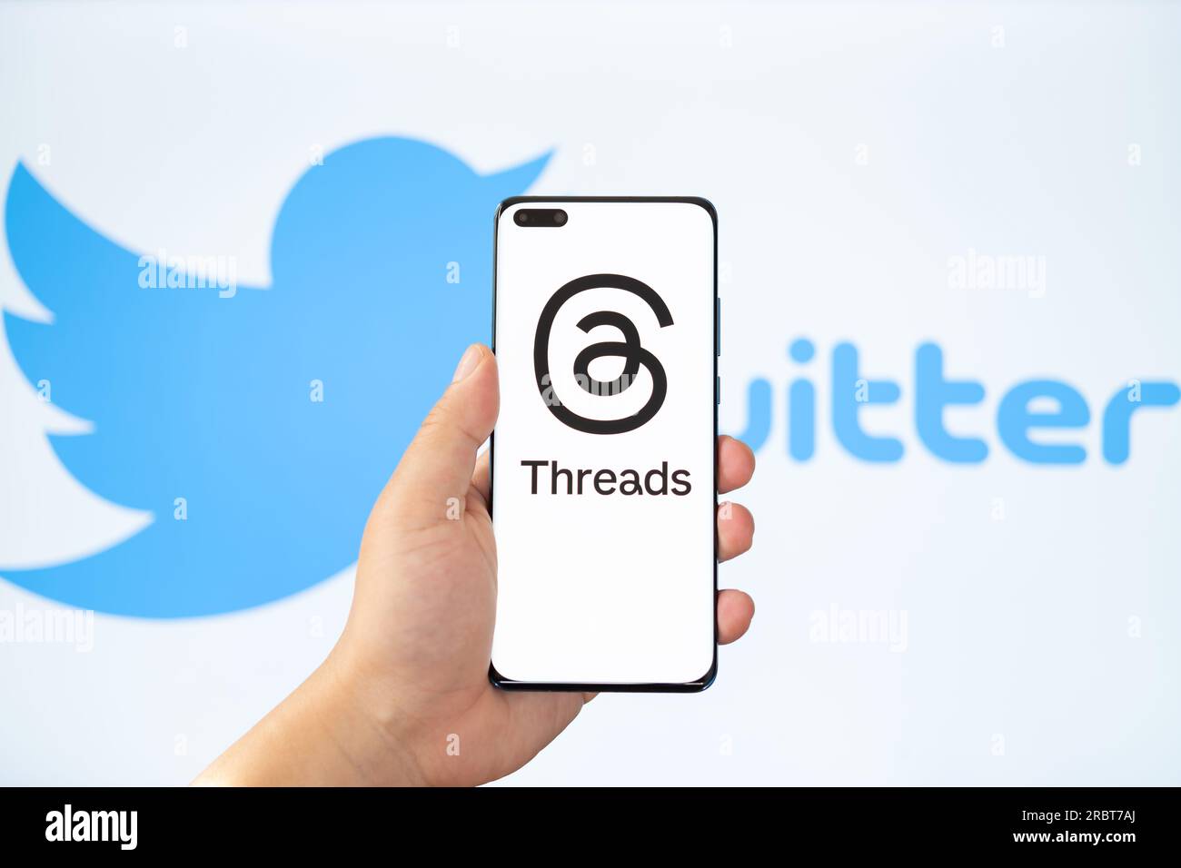 ZHONGSHAN China-Juli 11,2023: Hand hält ein Handy mit Thread-Logo, ein verschwommener Twitter-Hintergrund auf der Rückseite. Stockfoto