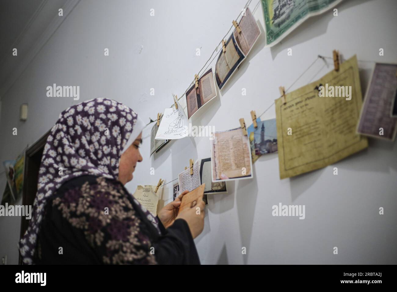 Gaza, Palästina. 10. Juli 2023. Eine palästinensische Frau hängt Bilder an das Seil, während sie Manuskripte und seltene Bücher restauriert und digitalisiert. Sie arbeitet im Labor innerhalb der Stiftung „Eyes on Heritage“ für Studien, Forschung und Verlagswesen in Gaza. Palästinensische Frauen arbeiten an der Archivierung und Restaurierung alter, seltener historischer Manuskripte und Bücher in einem Labor, das von der British Library in London und dem Hill Museum finanziert wird. Kredit: SOPA Images Limited/Alamy Live News Stockfoto