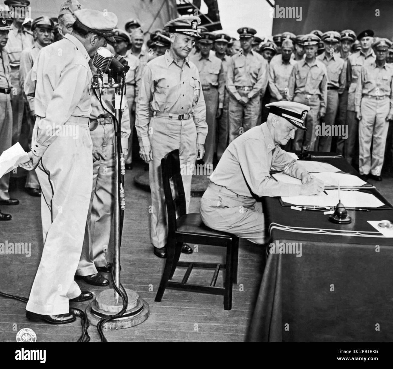 Tokio, Japan: 1. September 1945 Flottenadmiral Chester Nimitz signiert während der japanischen Kapitulationszeremonie an Bord der USS Missouri in der Bucht von Tokio für die Vereinigten Staaten. General der Armee Douglas MacArthur steht links am Mikrofon. Stockfoto